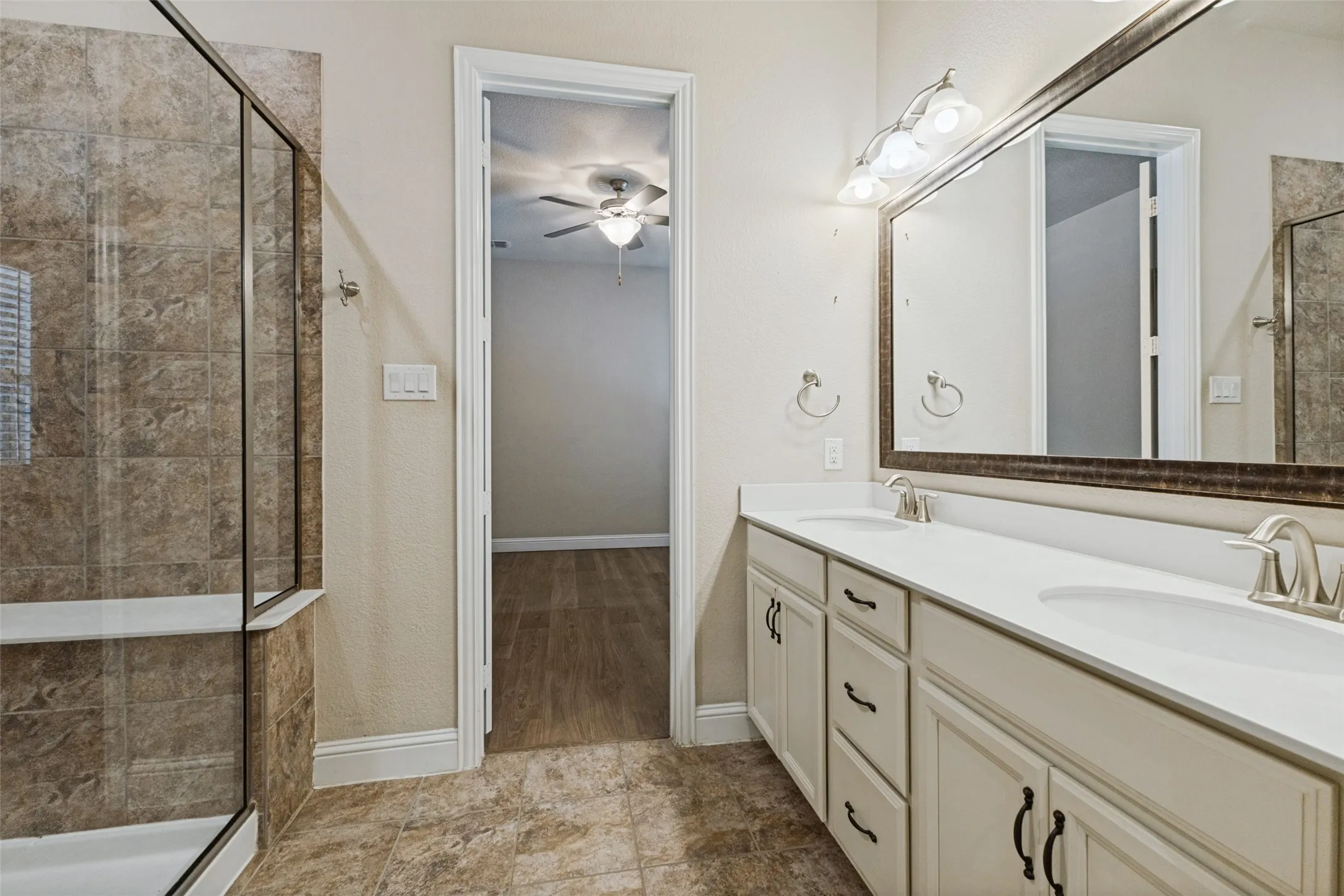 Dual vanity, decorative framed mirror, attached wall sconce lighting, and a walk-in shower with tiled walls and a glass enclosure