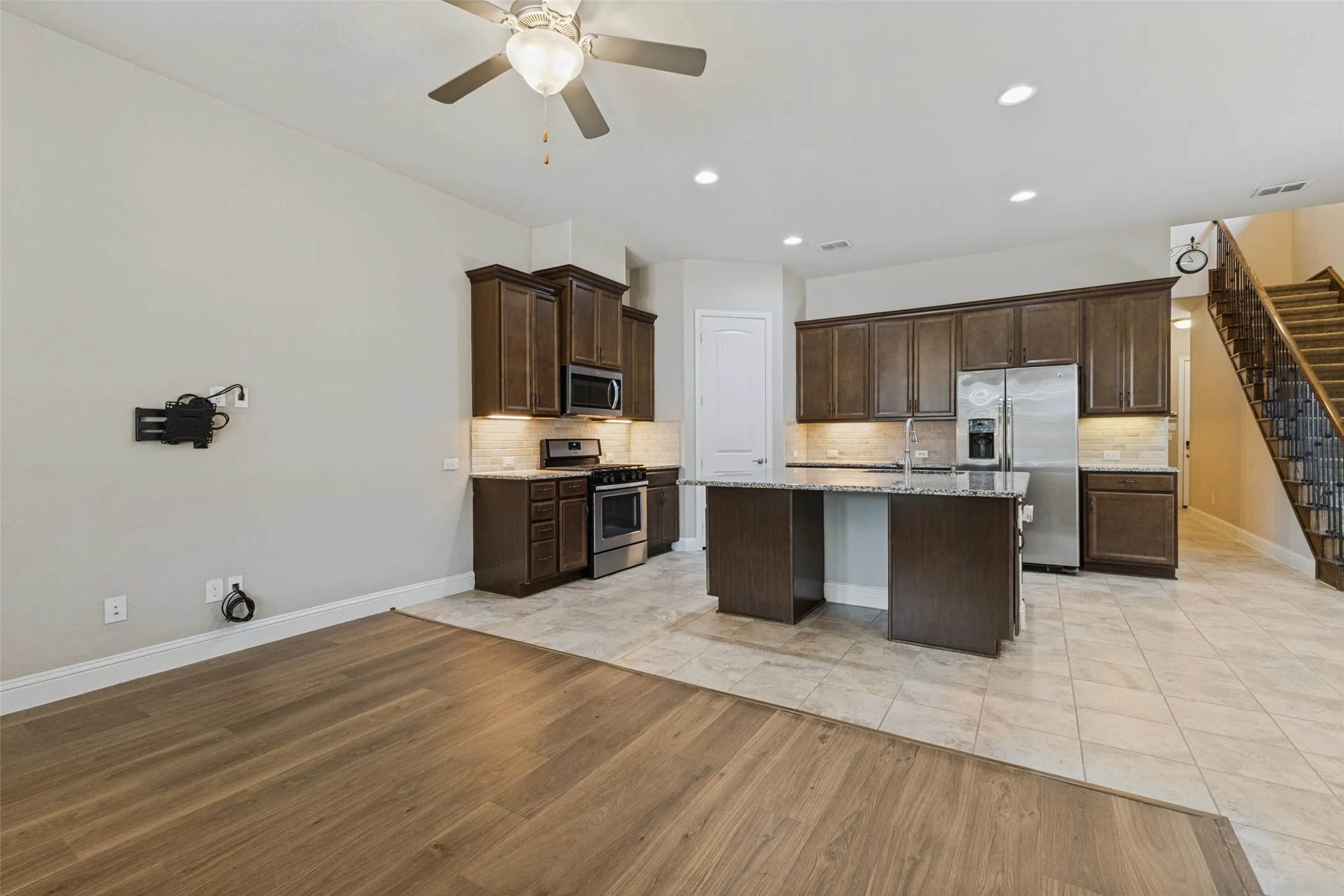 Open-concept layout featuring wood-flooring, a kitchen island with granite countertop, stainless steel appliances, and dark wood cabinetry