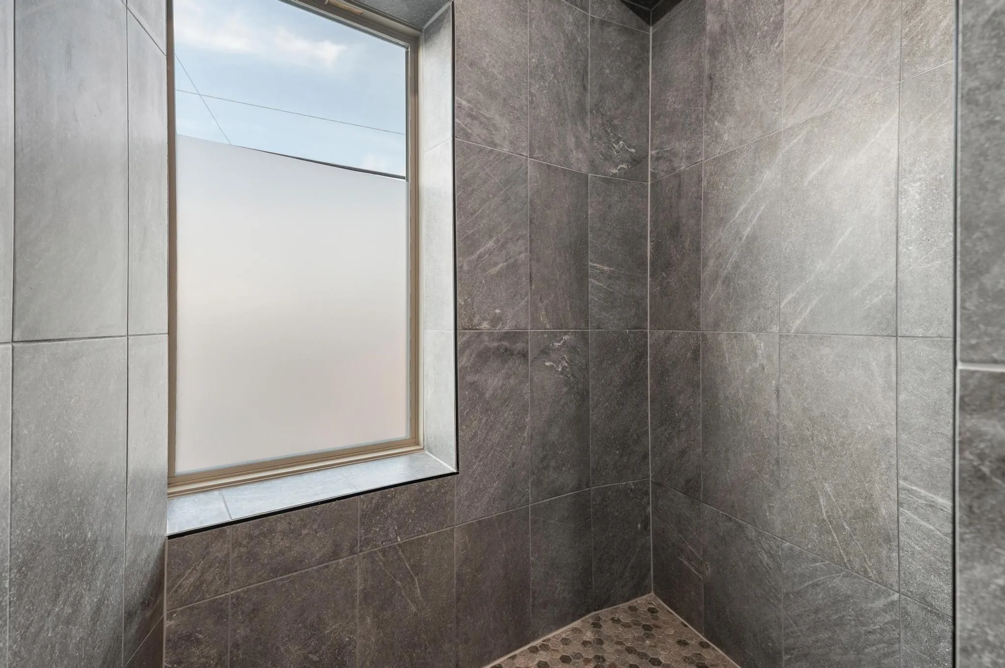 Shower enclosure featuring large format stone-look tile walls, a frosted window, and a mosaic tile floor