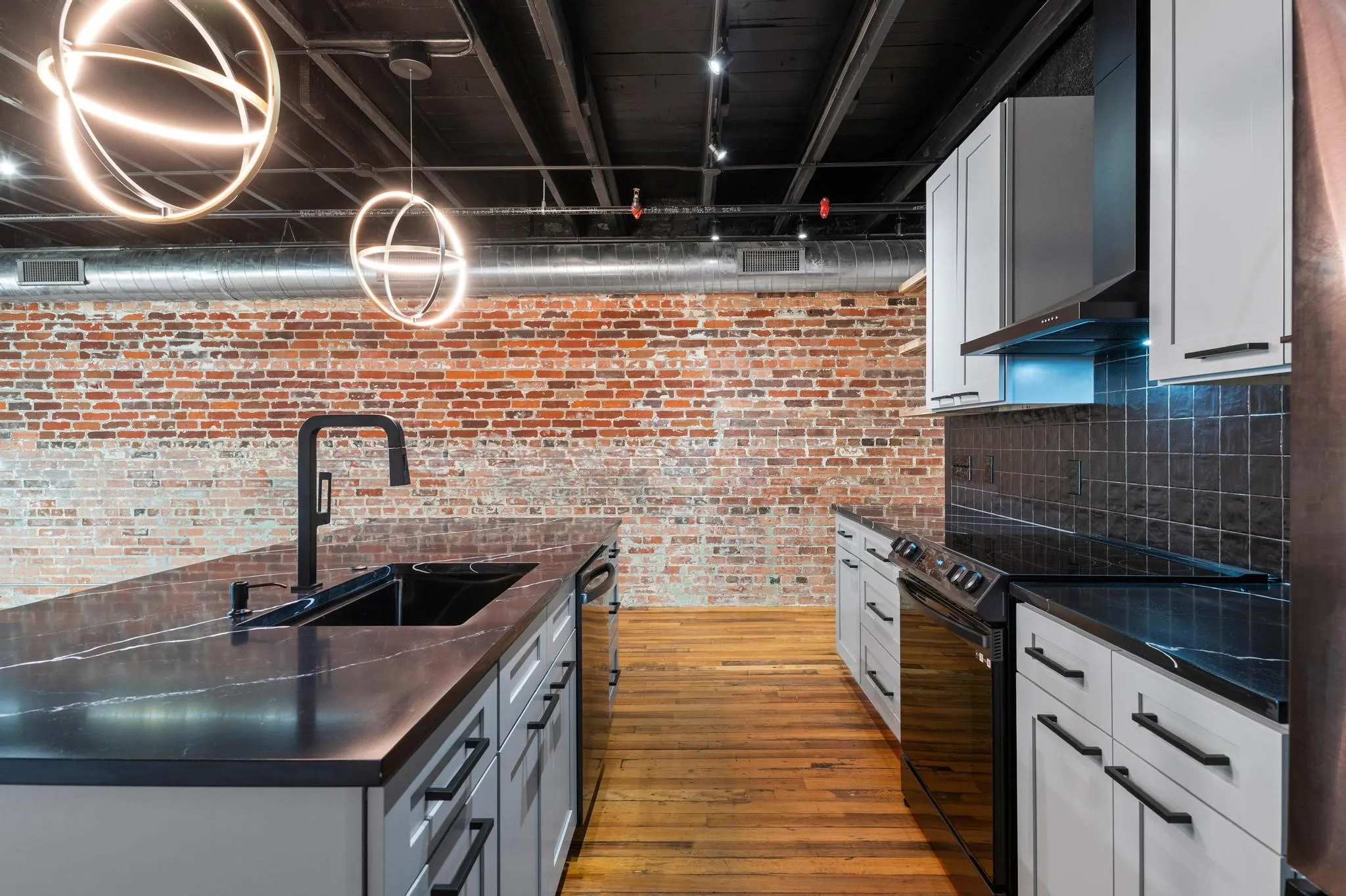 Kitchen featuring a large island with black sink and faucet, light-toned cabinetry, dark countertops, and a subway tile backsplash