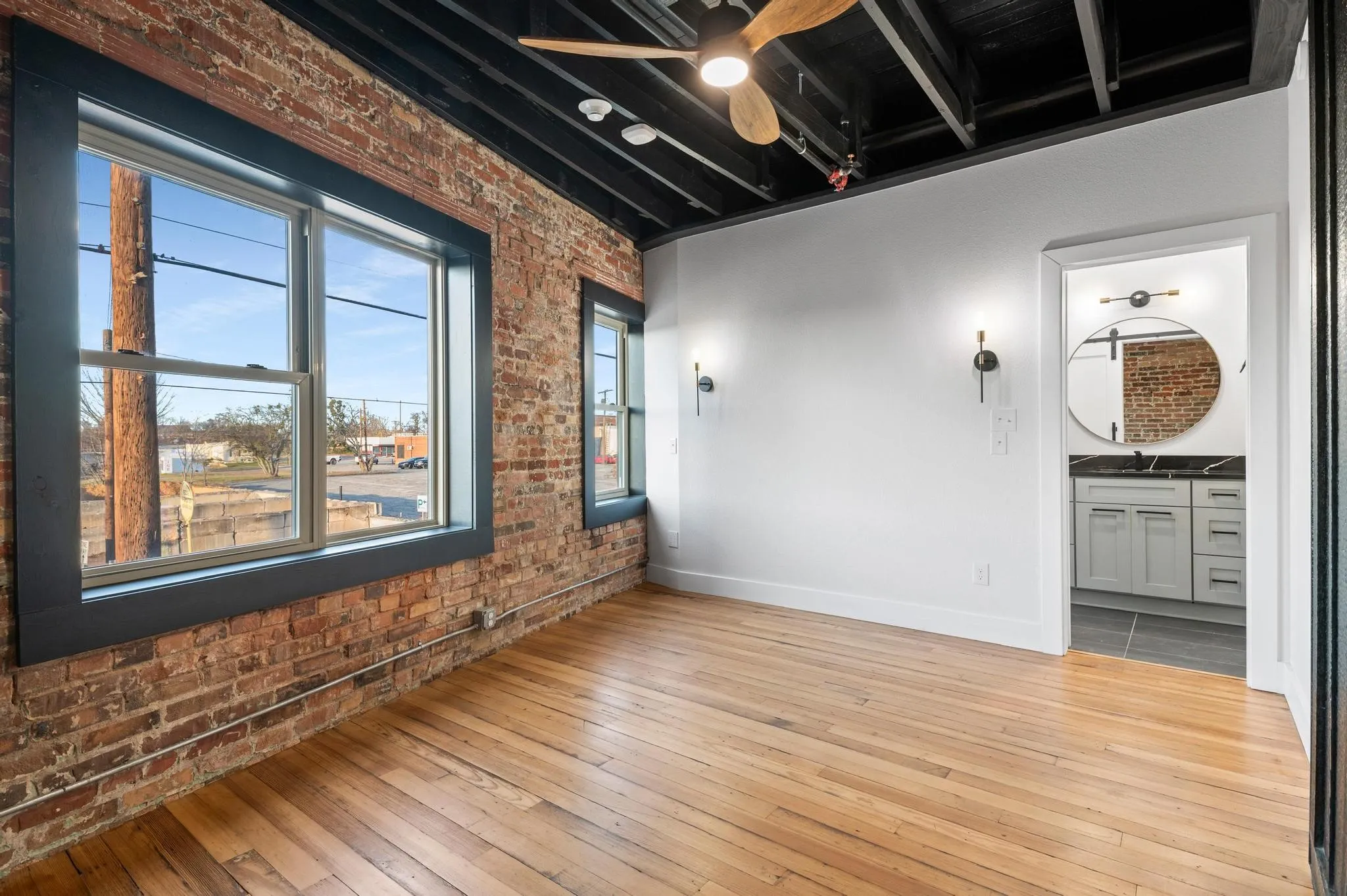 Exposed brick wall with large windows, wood-finish flooring, and industrial-style ceiling fan