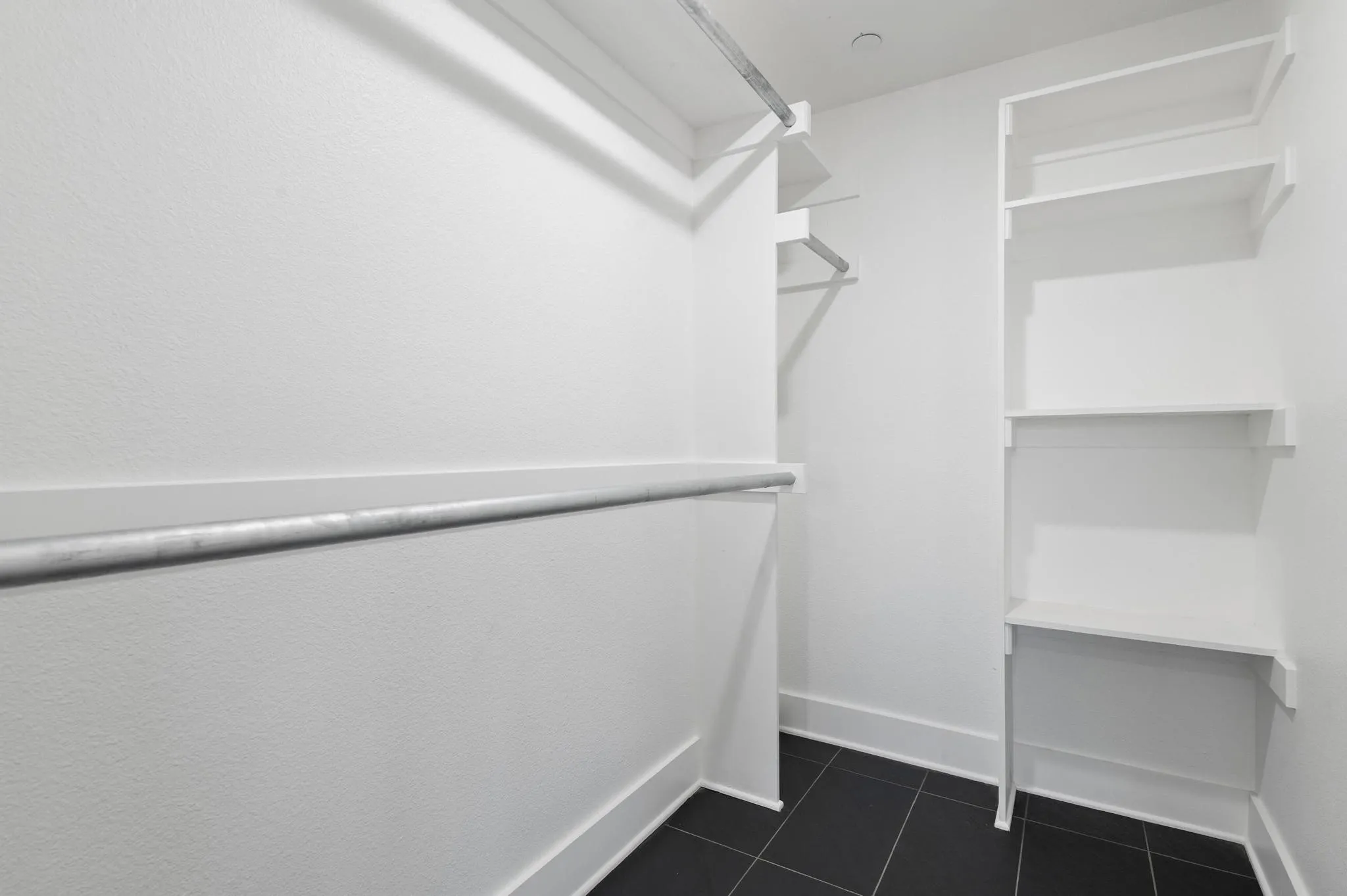 Walk-in closet with multiple hanging rods, built-in shelving, and dark tile flooring