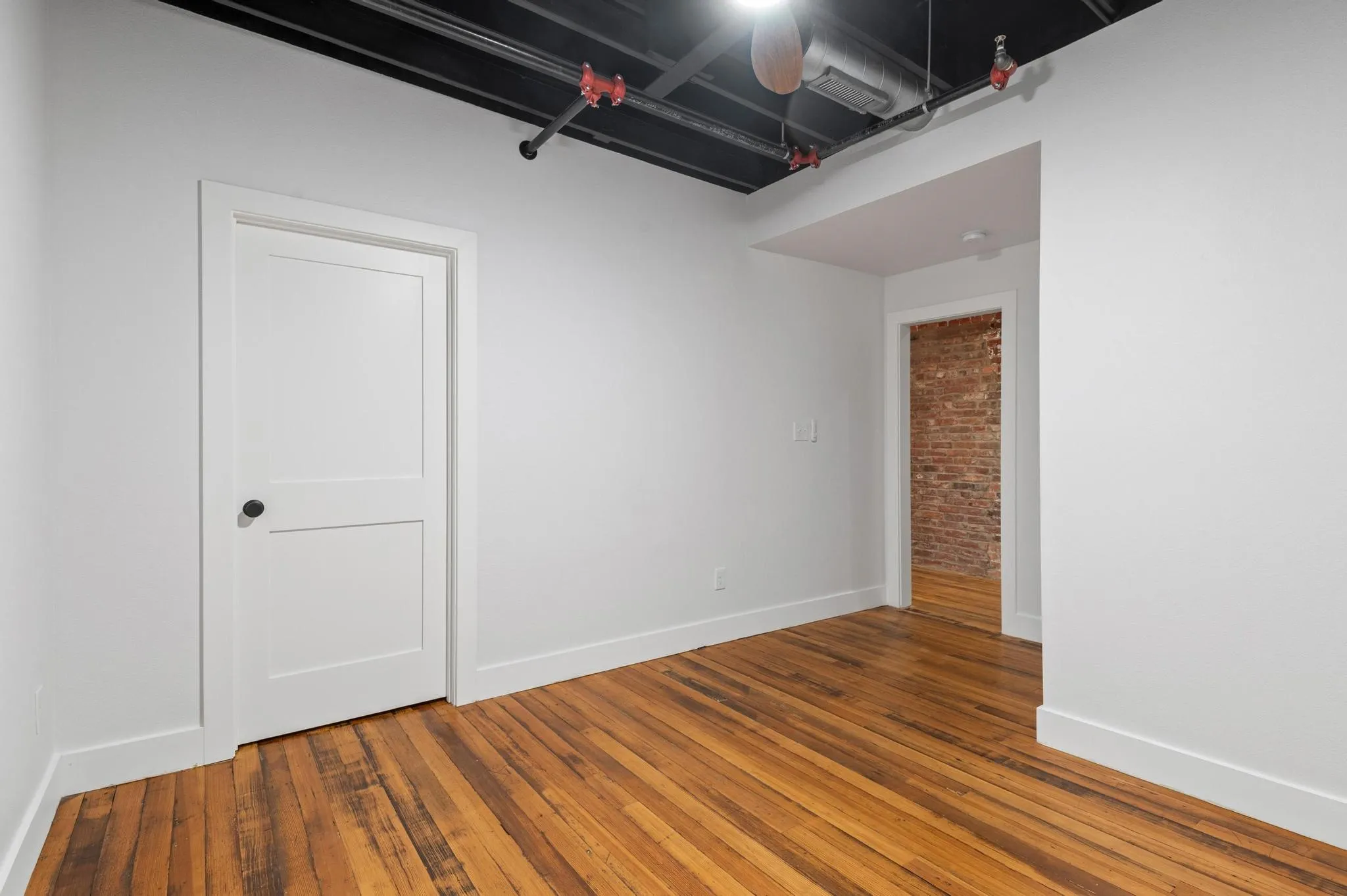 Hardwood flooring, exposed brick wall, white trim, recessed lighting, and exposed ceiling ductwork