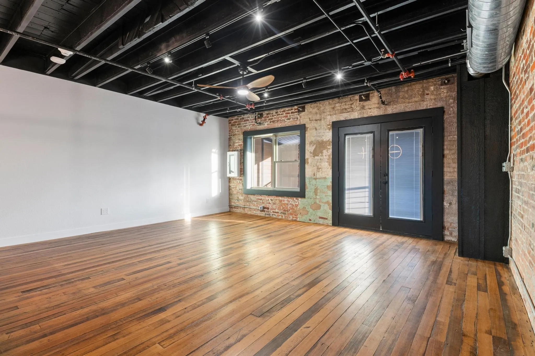 Exposed brick walls, wood-finish flooring, black-framed French doors, black exposed ceiling, and track lighting