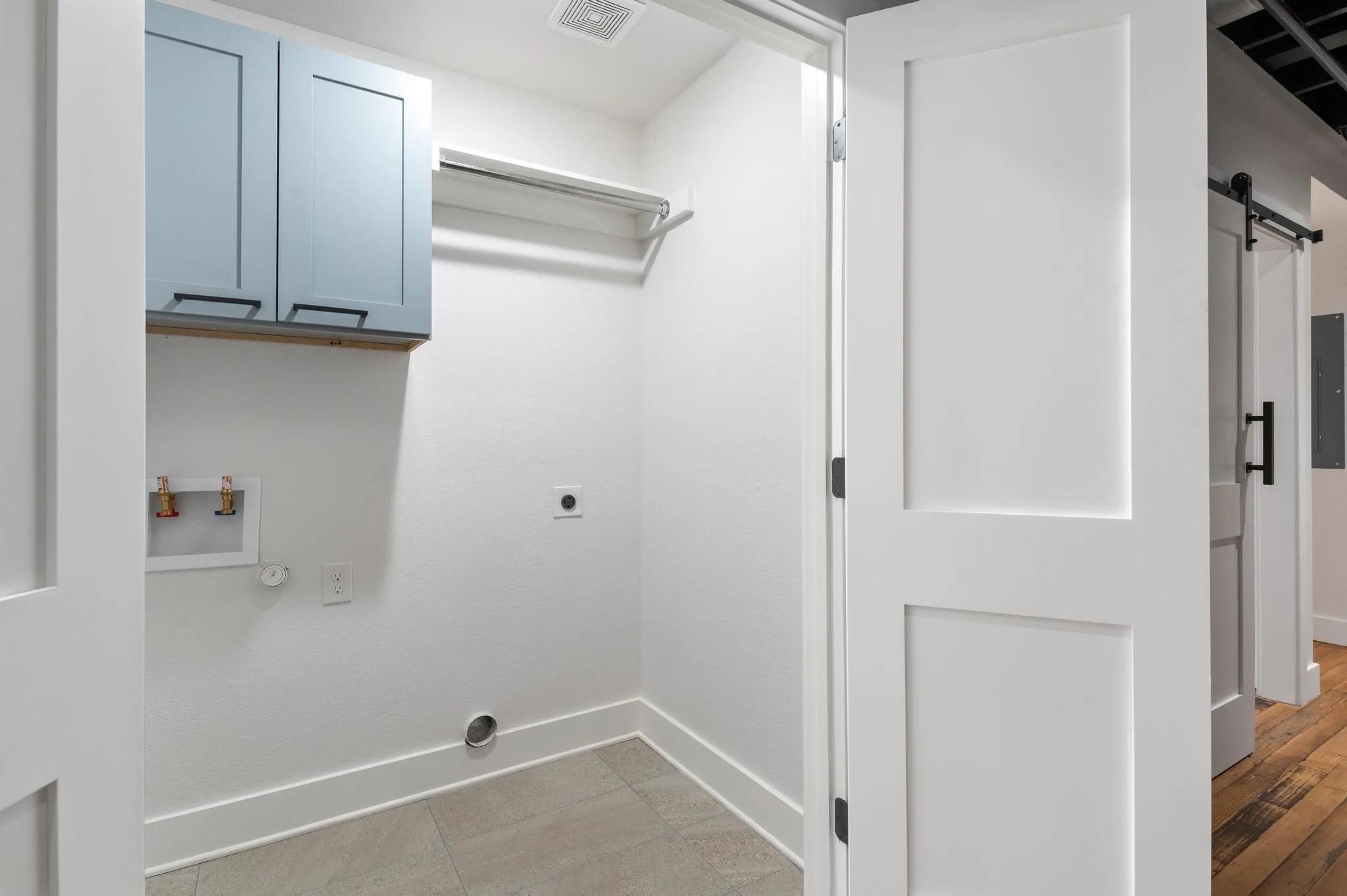 Laundry area with light blue cabinetry, clothes hanging rod, and neutral-toned floor tile