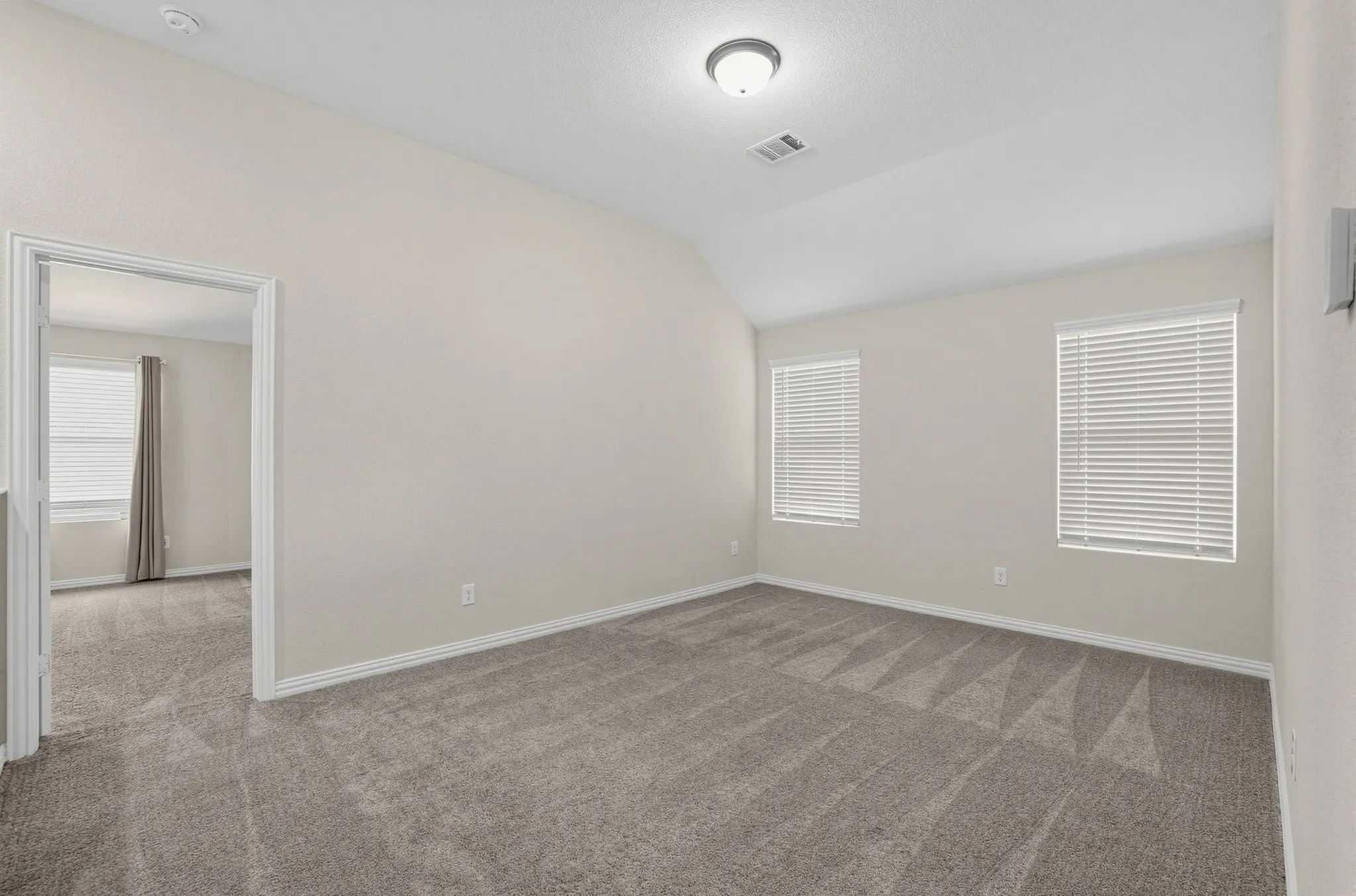Sloped ceiling design, two windows with horizontal blinds, flush mount ceiling light fixture, and neutral wall paint