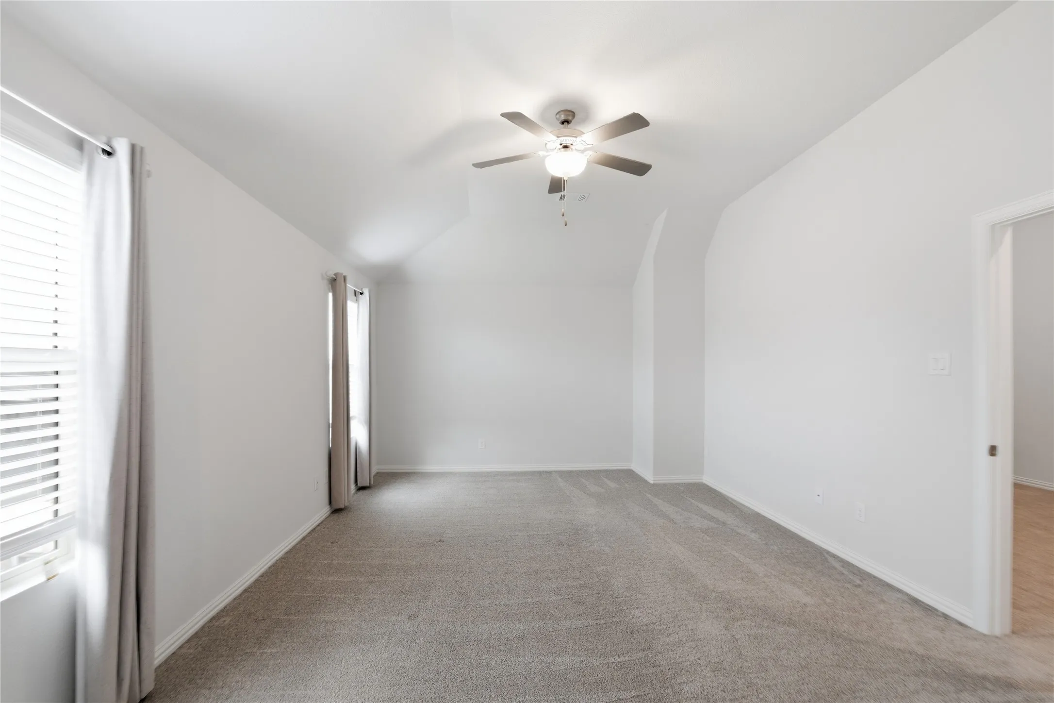 Carpeted room featuring a ceiling fan with integrated lighting, multiple windows with blinds, and white walls