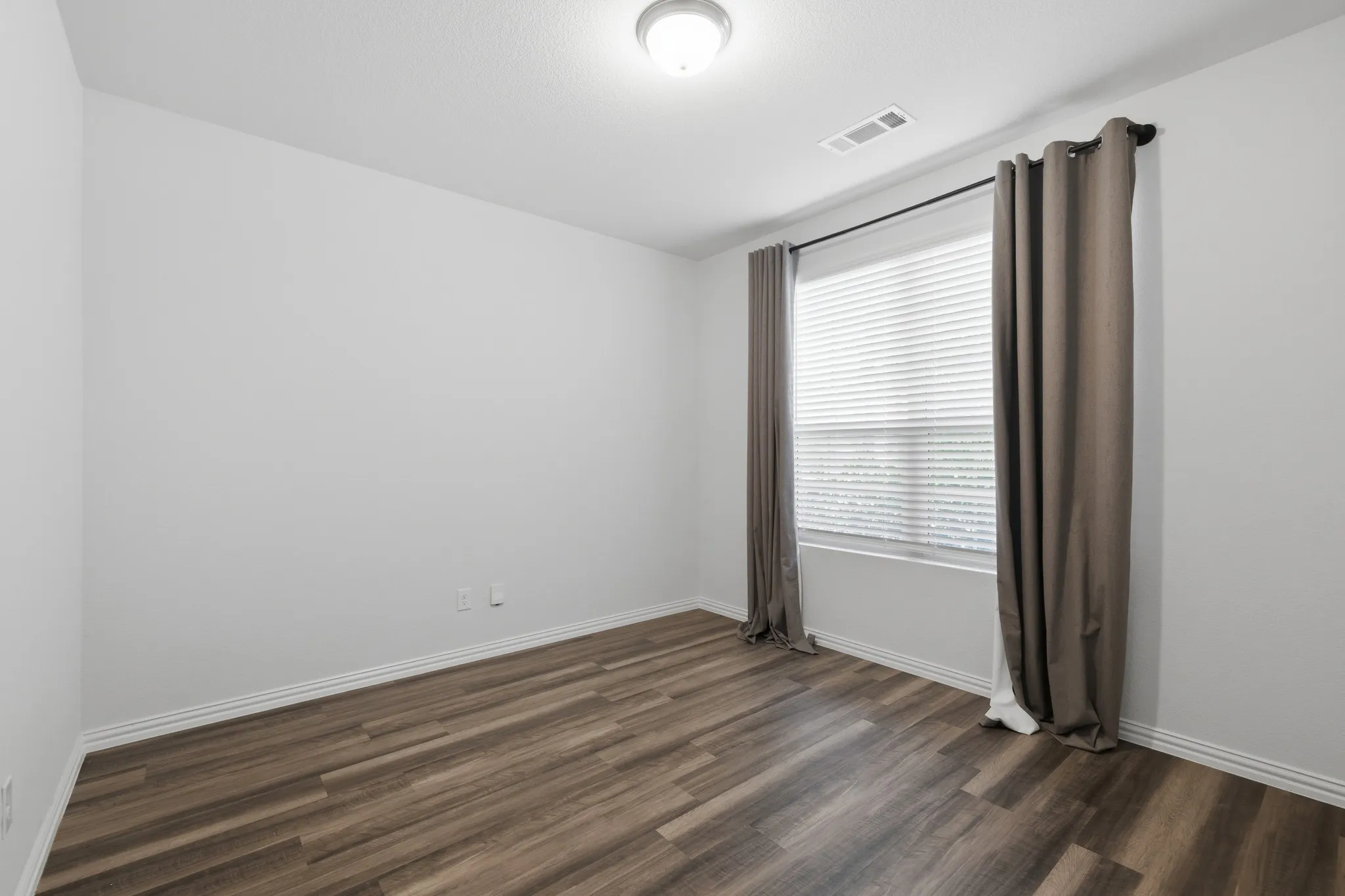Wood-finish flooring with white baseboards, bright white walls, and a window with blinds