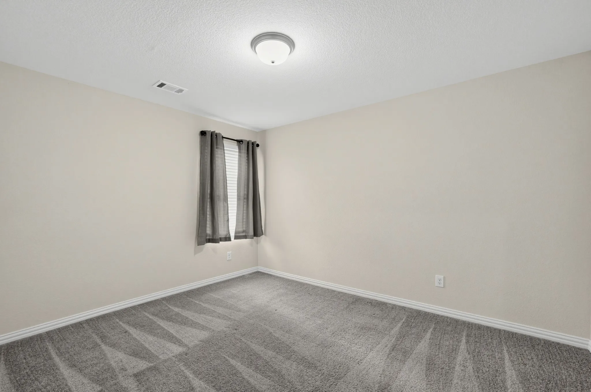Neutral wall tones with a window, ceiling light fixture, and patterned carpeting