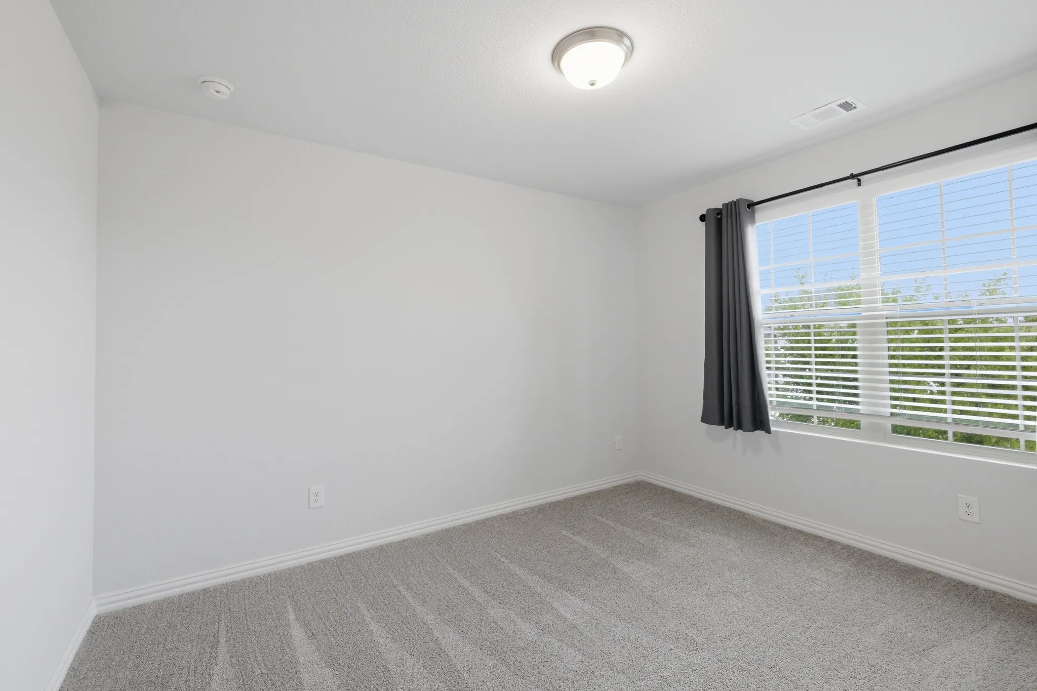 Broad window with blinds, light-toned wall-to-wall carpeting, white baseboards, and a flush mount ceiling light fixture