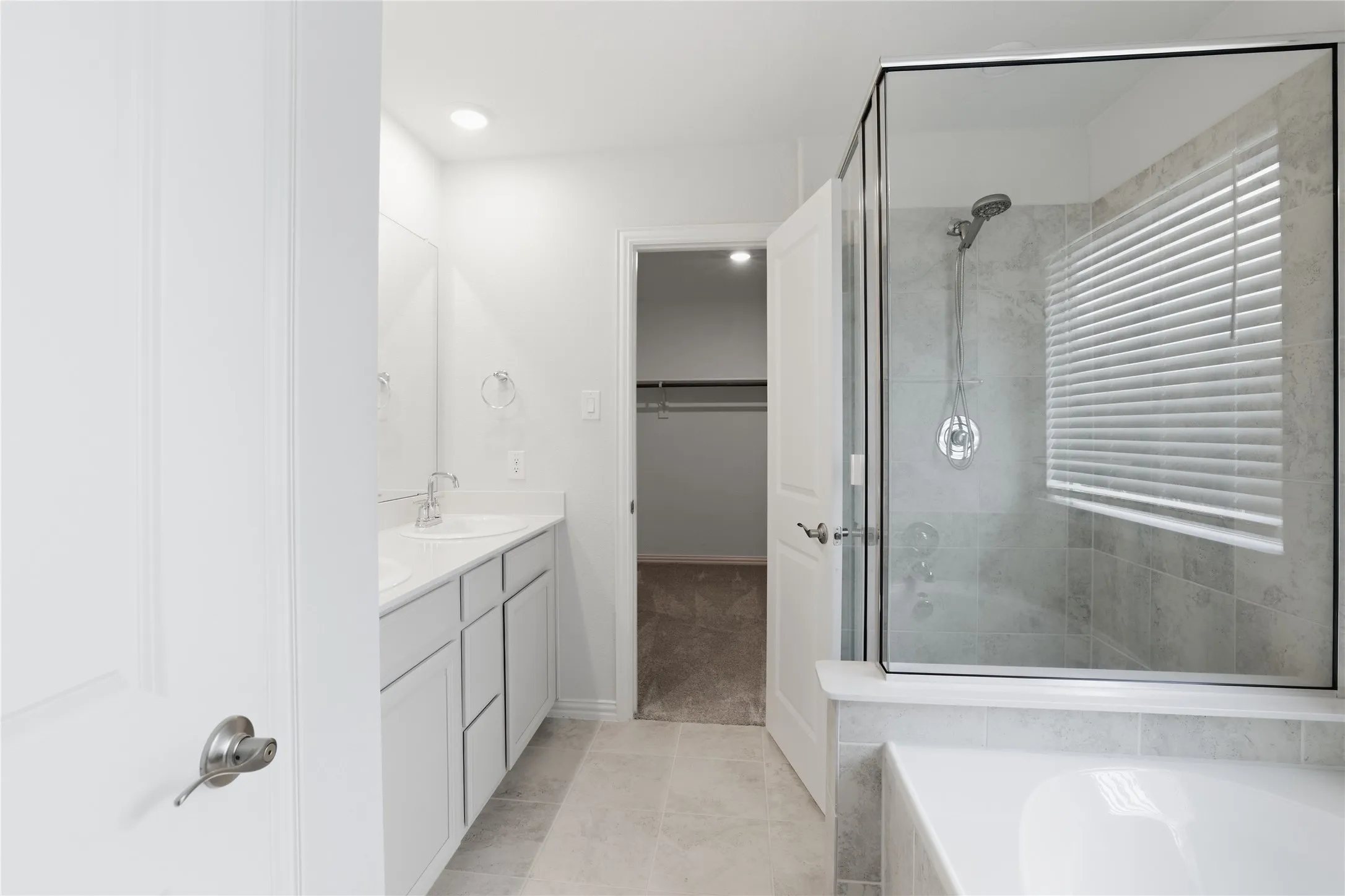 Dual vanity with undermount sinks, frameless glass shower enclosure, built-in bathtub, and tiled flooring