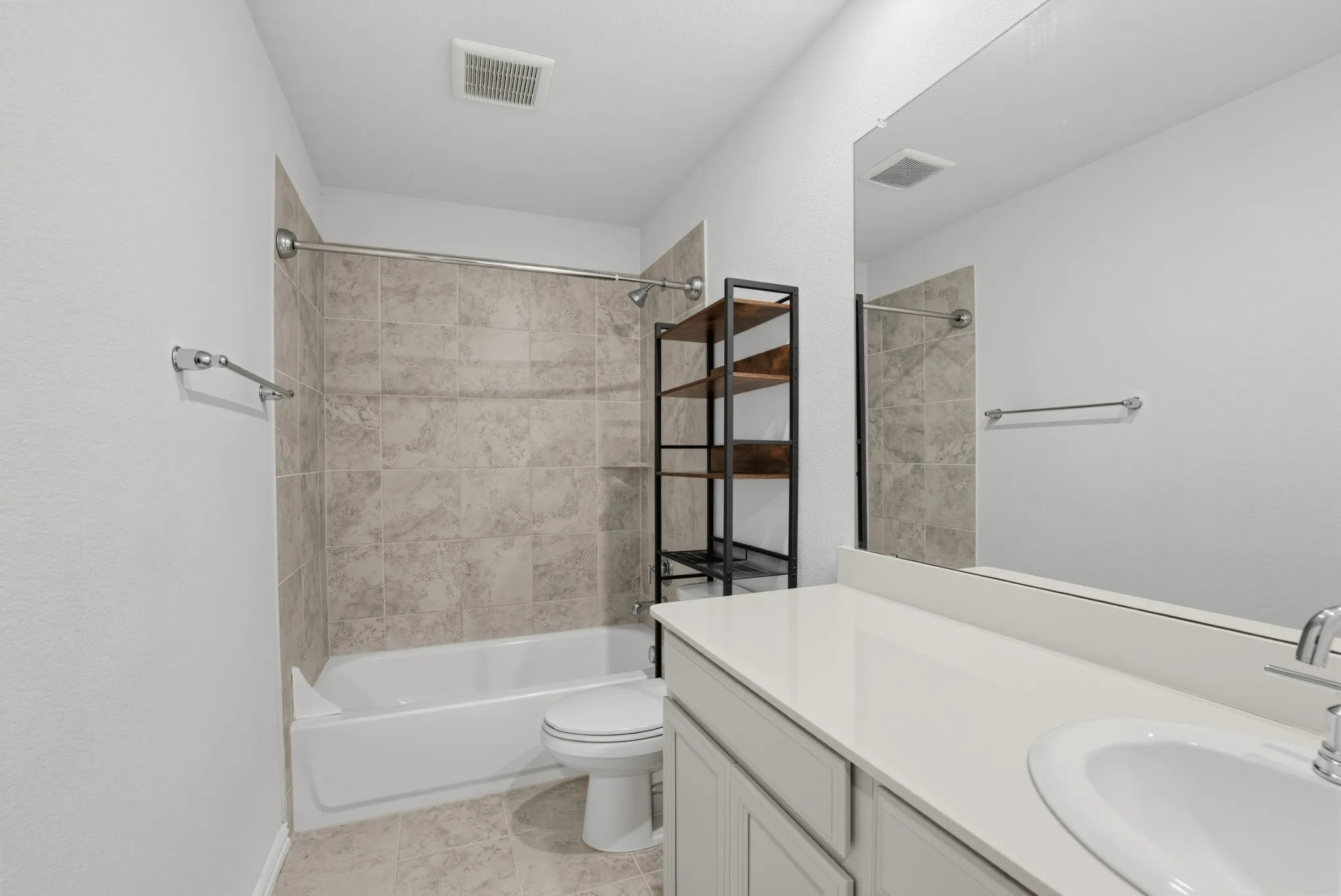 Bathroom featuring a white vanity with an integrated sink, a large mirror, a bathtub with a tiled surround, and tile flooring