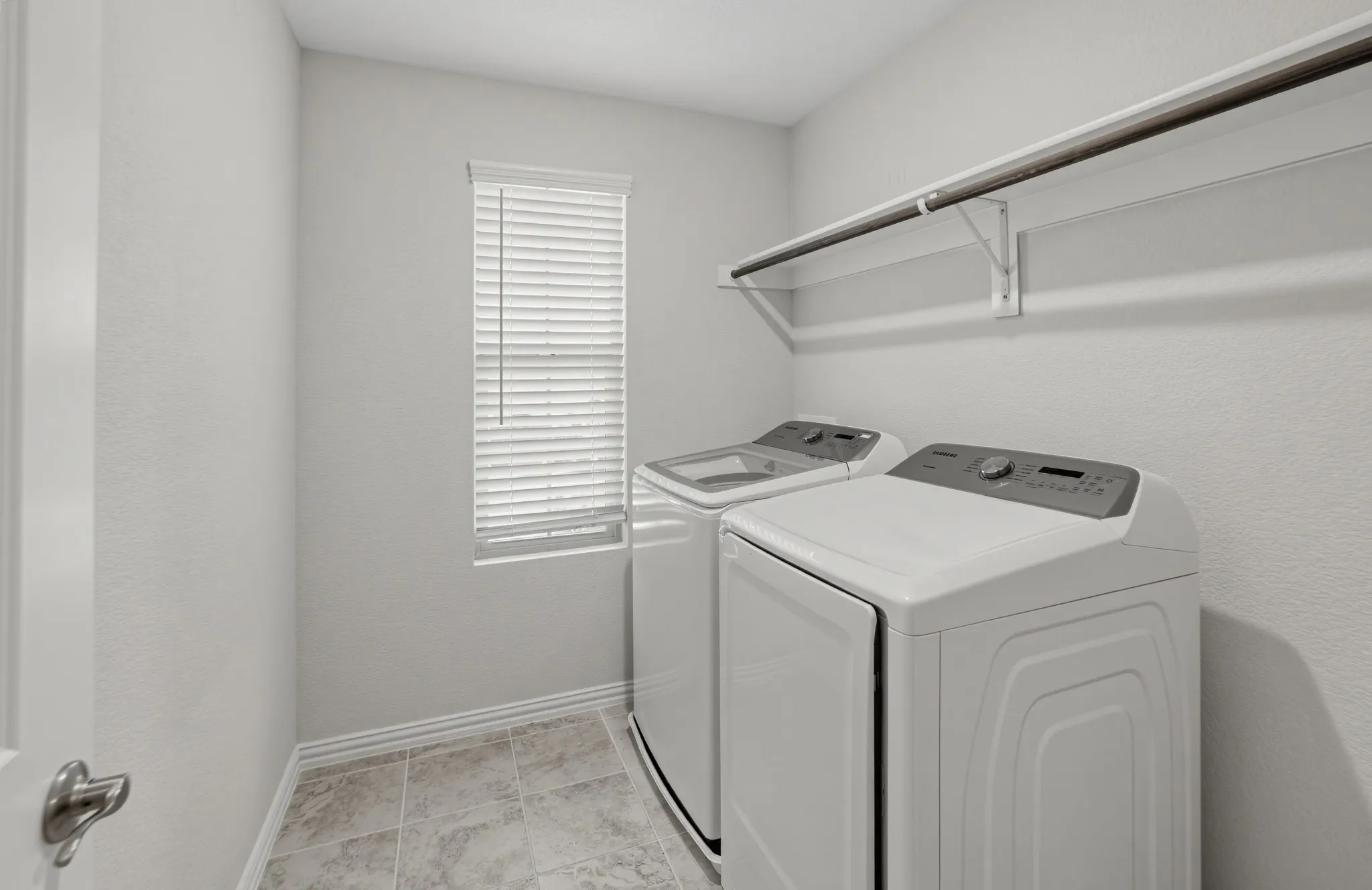 Laundry area featuring tile flooring, a window with blinds, and an integrated shelf with a hanging rod