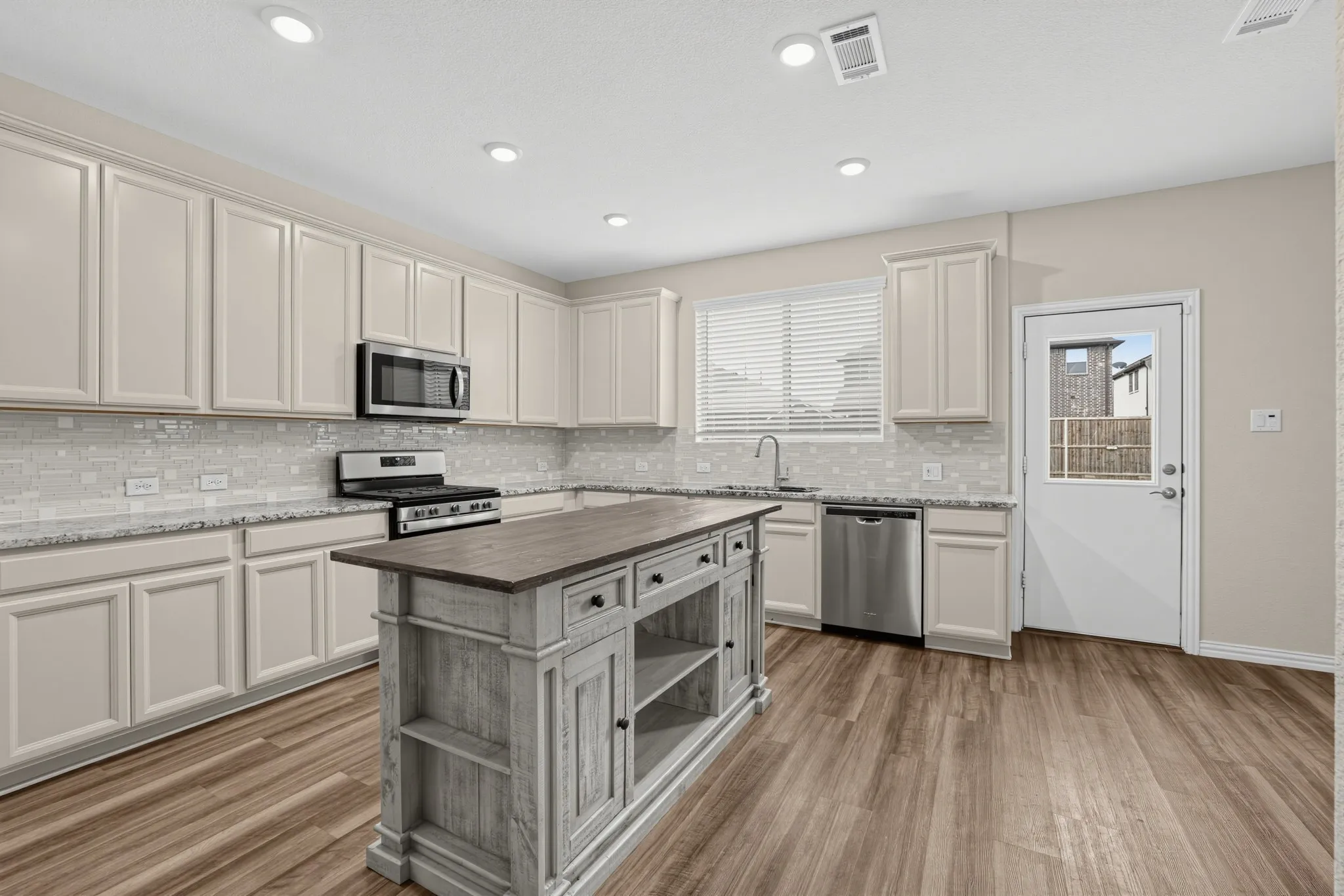Kitchen featuring wood-finish flooring, recessed lighting, a central island with distressed wood-finish countertop, stainless steel appliances, and light-colored cabinetry with granite countertops