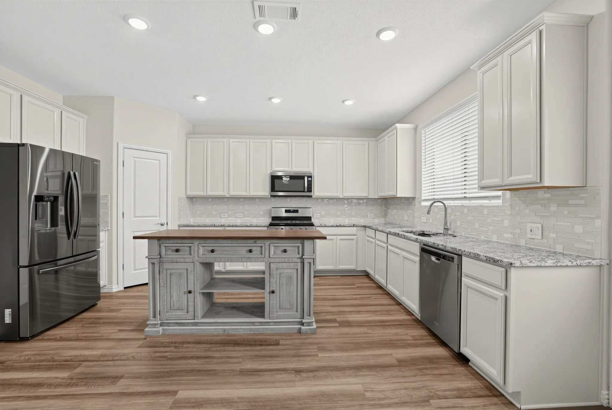 Kitchen featuring white cabinetry, light-toned countertops, a decorative center island with wood-finish top, and stainless steel appliances