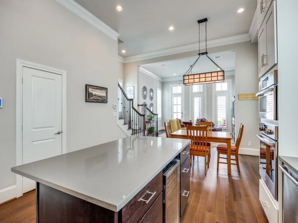 Kitchen island with a light-toned countertop, wood-finish flooring, built-in double oven, recessed lighting, and crown molding