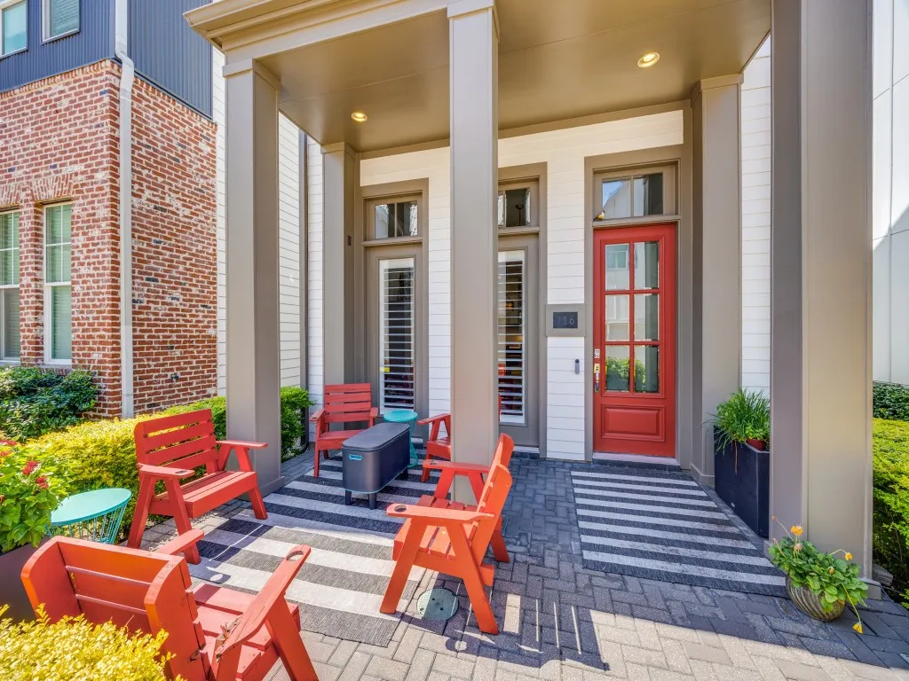 Covered entryway with brick paver flooring, a red paneled door with glass inserts, and a white siding exterior