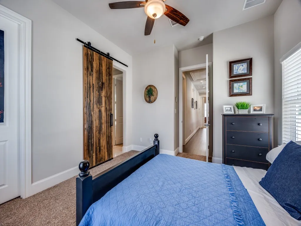 Barn door with black hardware, ceiling fan with integrated lighting, carpeted flooring, and window with blinds