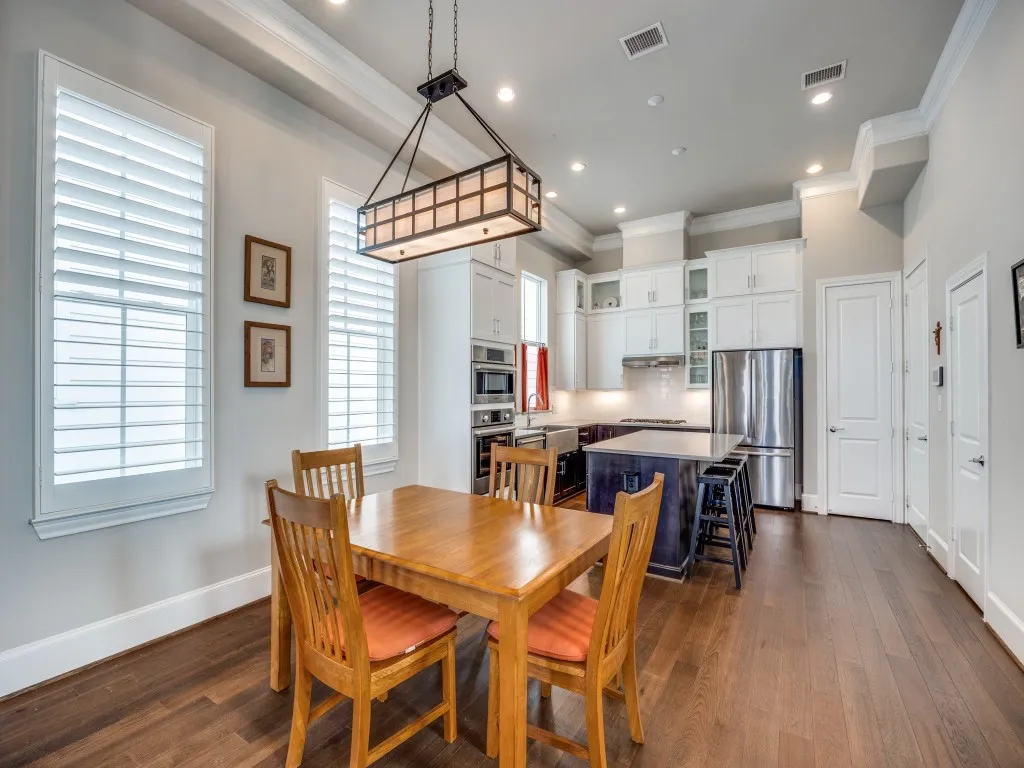 Open-concept living space with dark wood-finish flooring, white plantation shutters, and a kitchen featuring white cabinetry, an island with seating, and stainless steel appliances