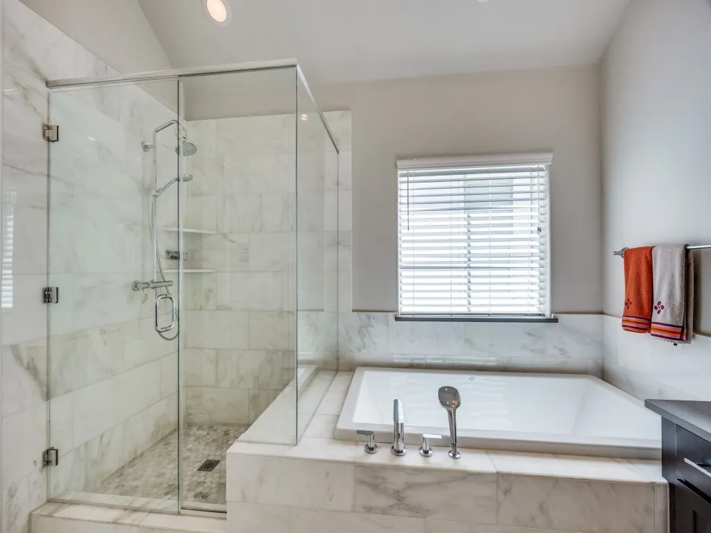 Glass-enclosed shower with a rainfall showerhead and handheld sprayer, large soaking tub with deck-mounted fixtures, and tiled surround