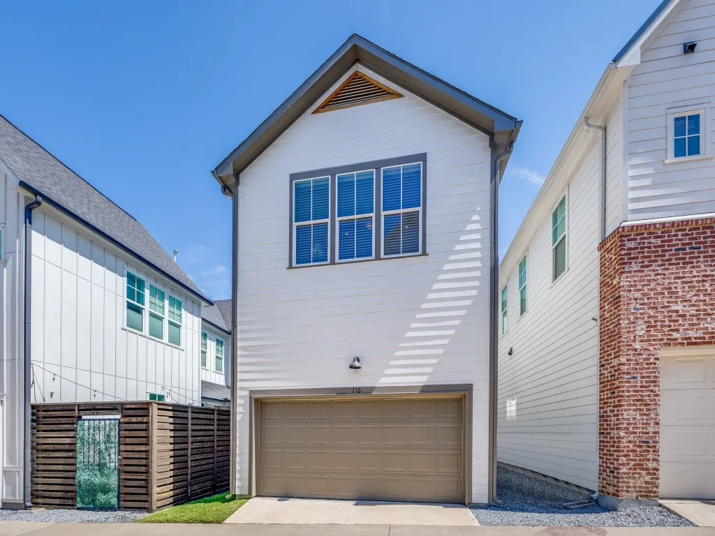 White vertical siding, upper-level windows with dark trim, attached garage with a tan door, and a horizontal slatted privacy fence