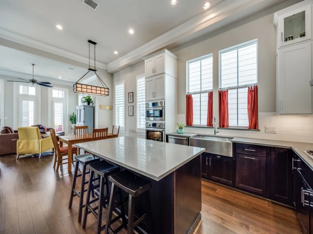 Kitchen featuring a central island with countertop seating, stainless steel apron-front sink, light-toned countertops, dark wood-finish lower cabinetry, and recessed lighting