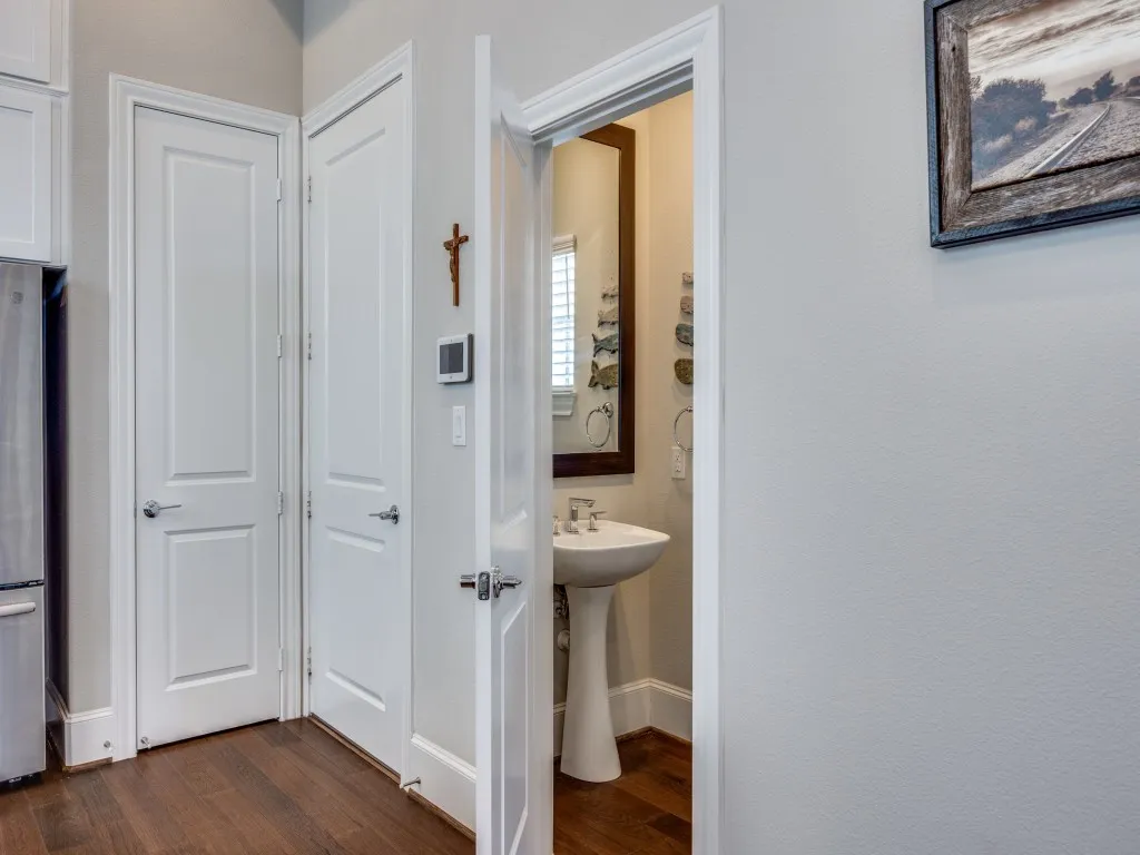 Pedestal sink with a polished chrome faucet, wood-finish flooring, and white interior doors