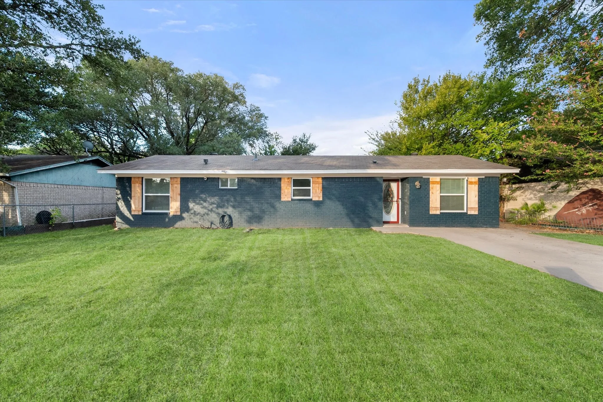 Ranch style house featuring painted brick exterior, wood window shutters and concrete driveway.