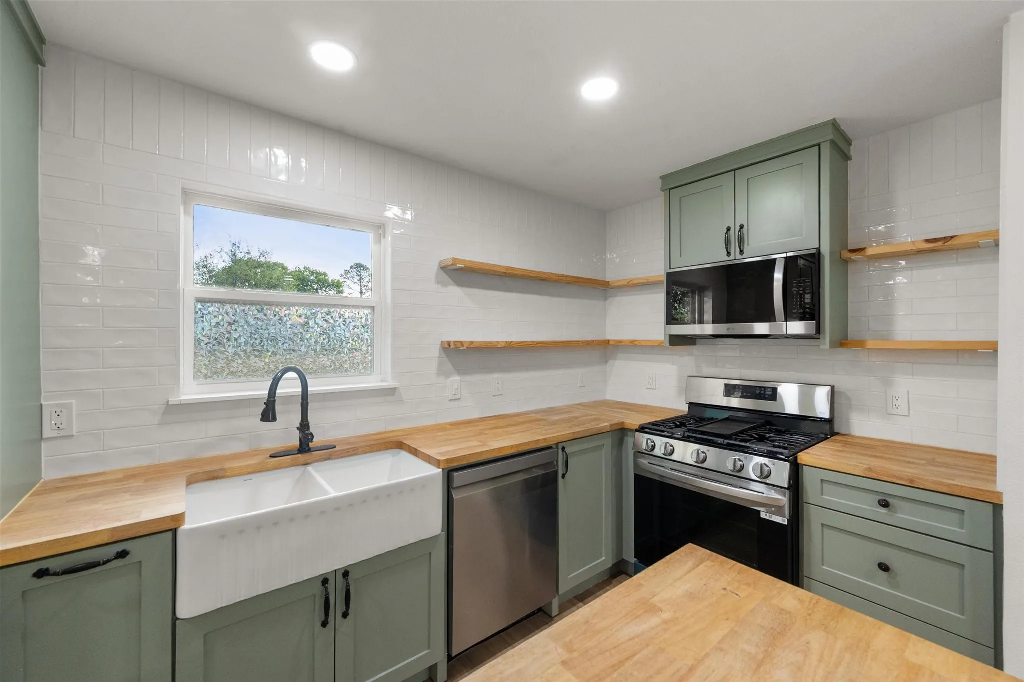 Hardwood butcher block countertops, dual-farmhouse sink with matte black faucet, painted, shaker style cabinetry, white subway tile backsplash, SS appliances and LED Lights.