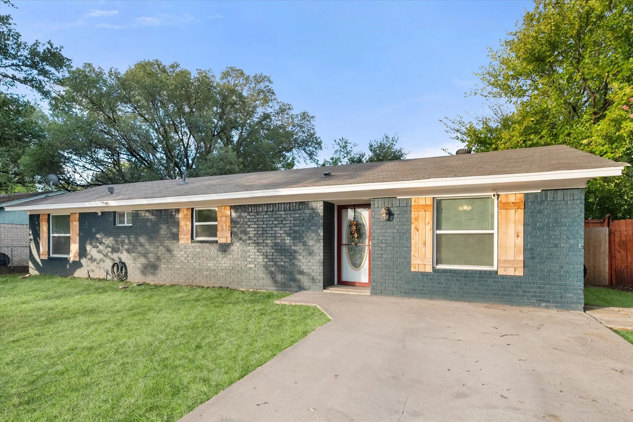 Ranch style house featuring painted brick exterior, wood window shutters and concrete driveway.