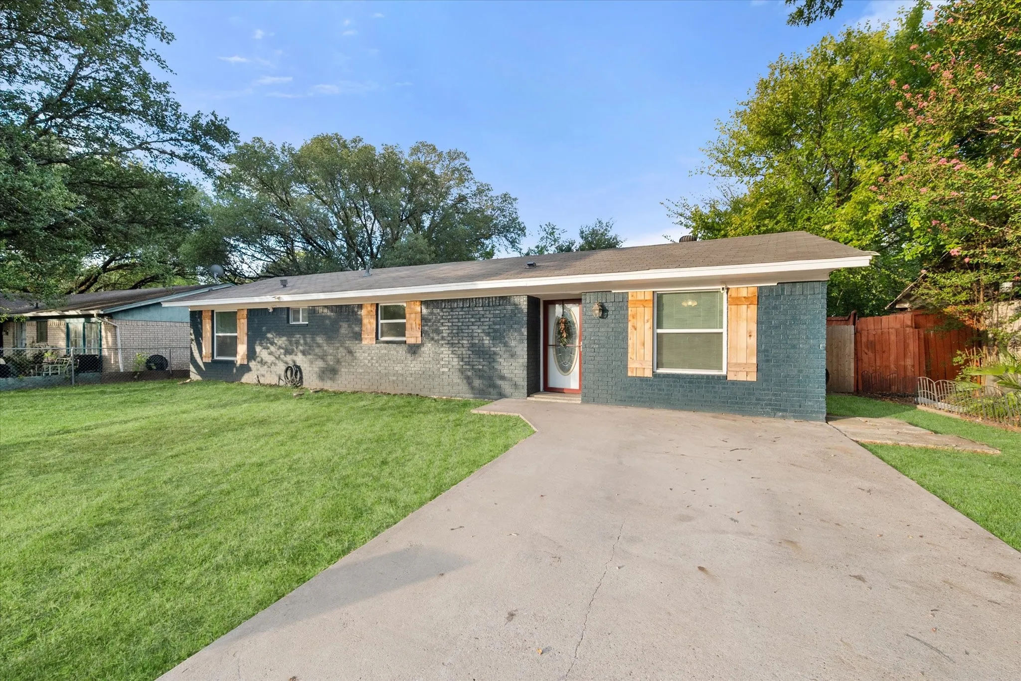 Ranch style house featuring painted brick exterior, wood window shutters and concrete driveway.