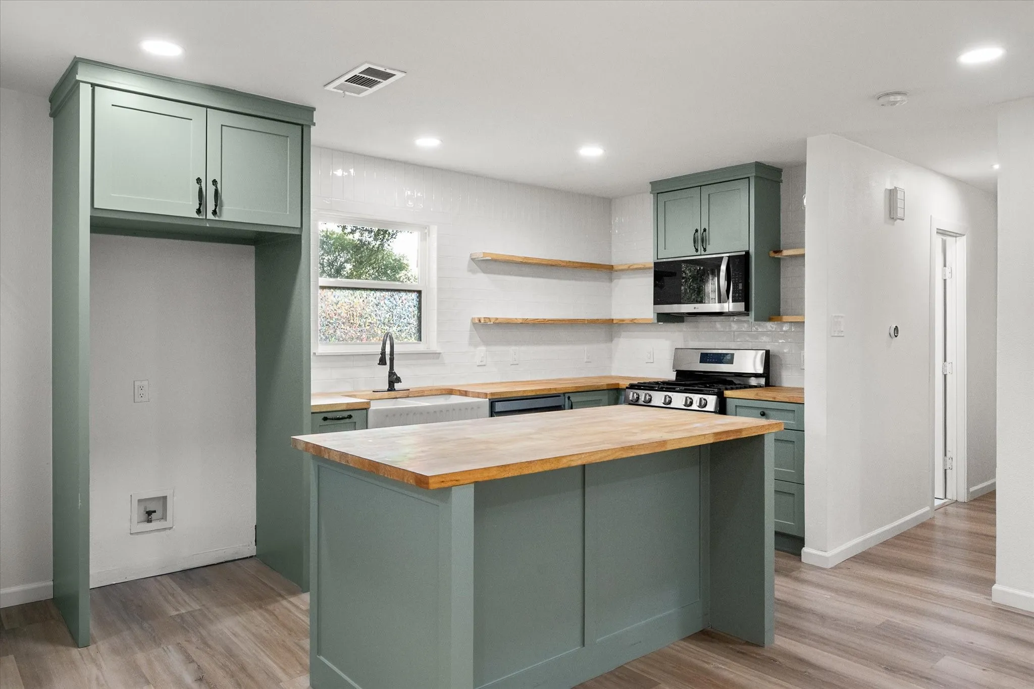 Kitchen area featuring wood looking ceramic flooring, upgraded kitchen shaker style painted cabinets, butcher style counters and LED lights.