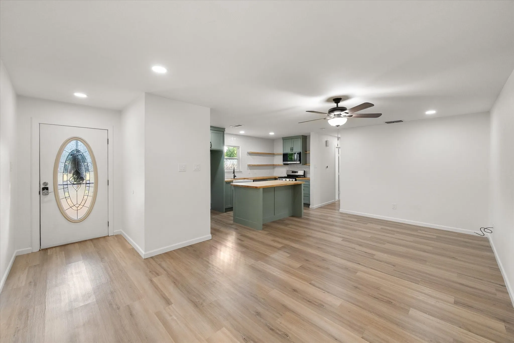 View of the entry, kitchen and living area featuring wood looking ceramic flooring upgraded kitchen painted cabinets and LED lights