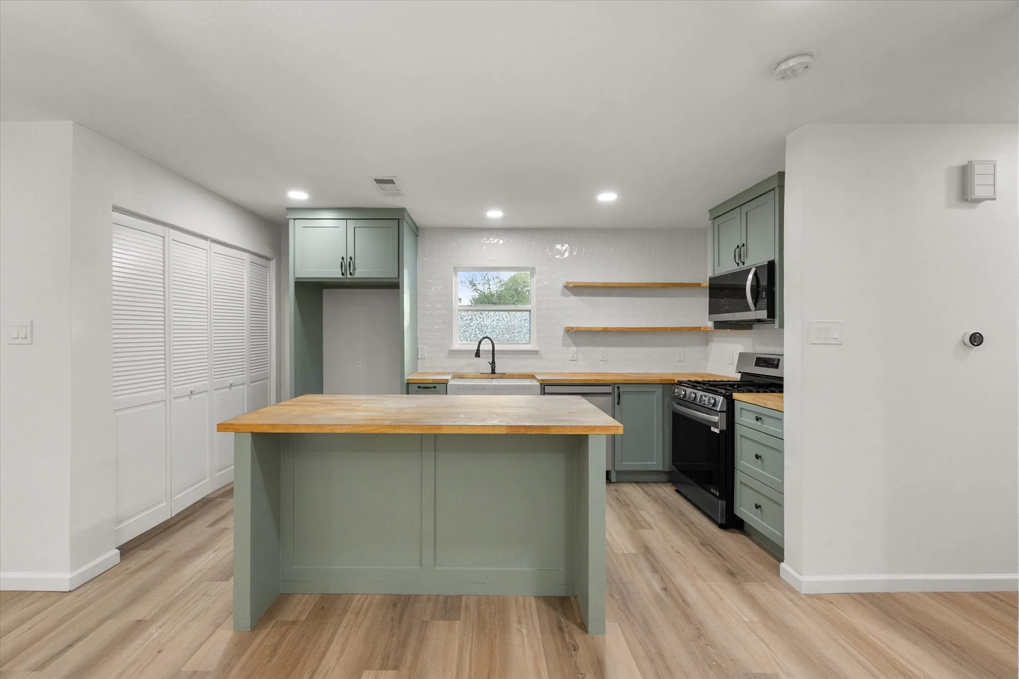 Kitchen area featuring wood looking ceramic flooring, upgraded kitchen painted cabinets, butcher style counters and LED lights.