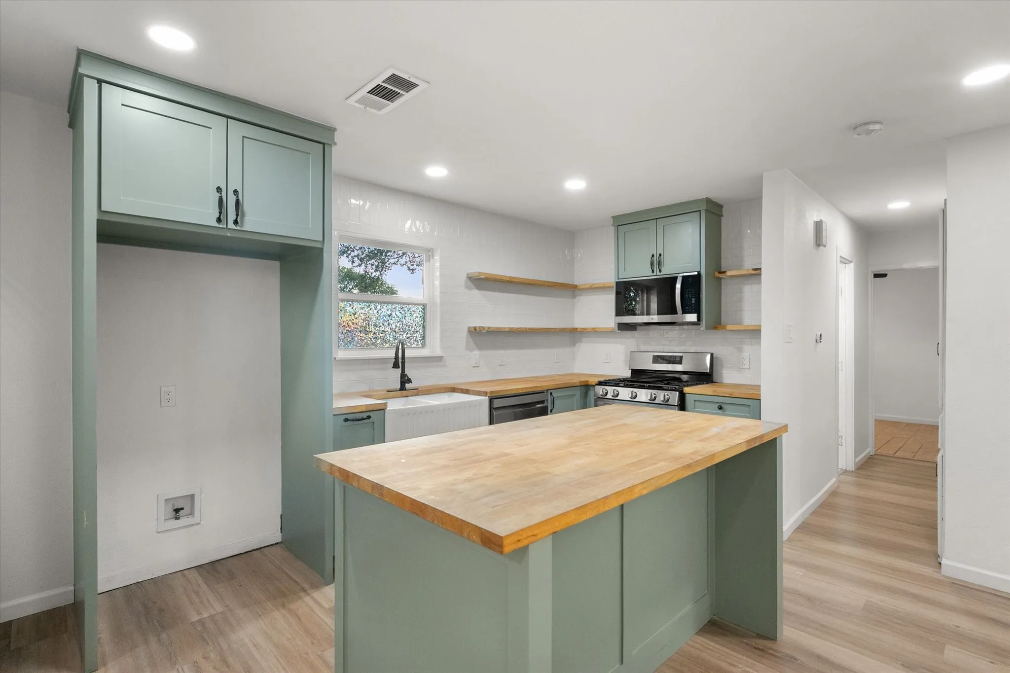 Kitchen area featuring wood looking ceramic flooring, upgraded kitchen painted cabinets,hardwood butcher style counters and island and LED lights.