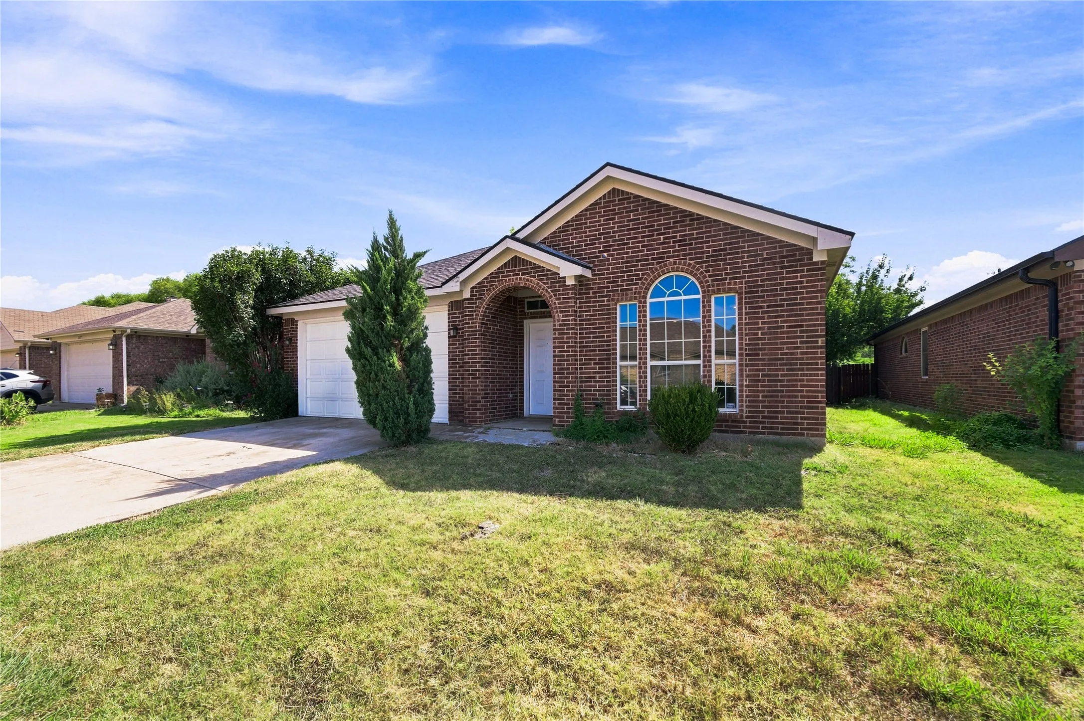 Brick exterior with arched entryway, multi-pane arched window, attached garage, and concrete driveway