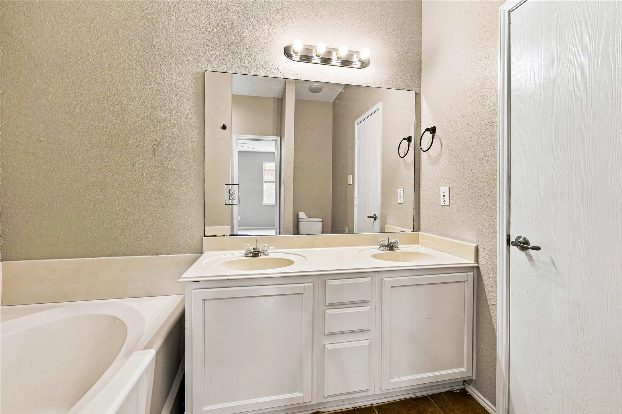 Dual vanity with integrated sinks, white cabinetry, large wall-mounted mirror, and a built-in bathtub