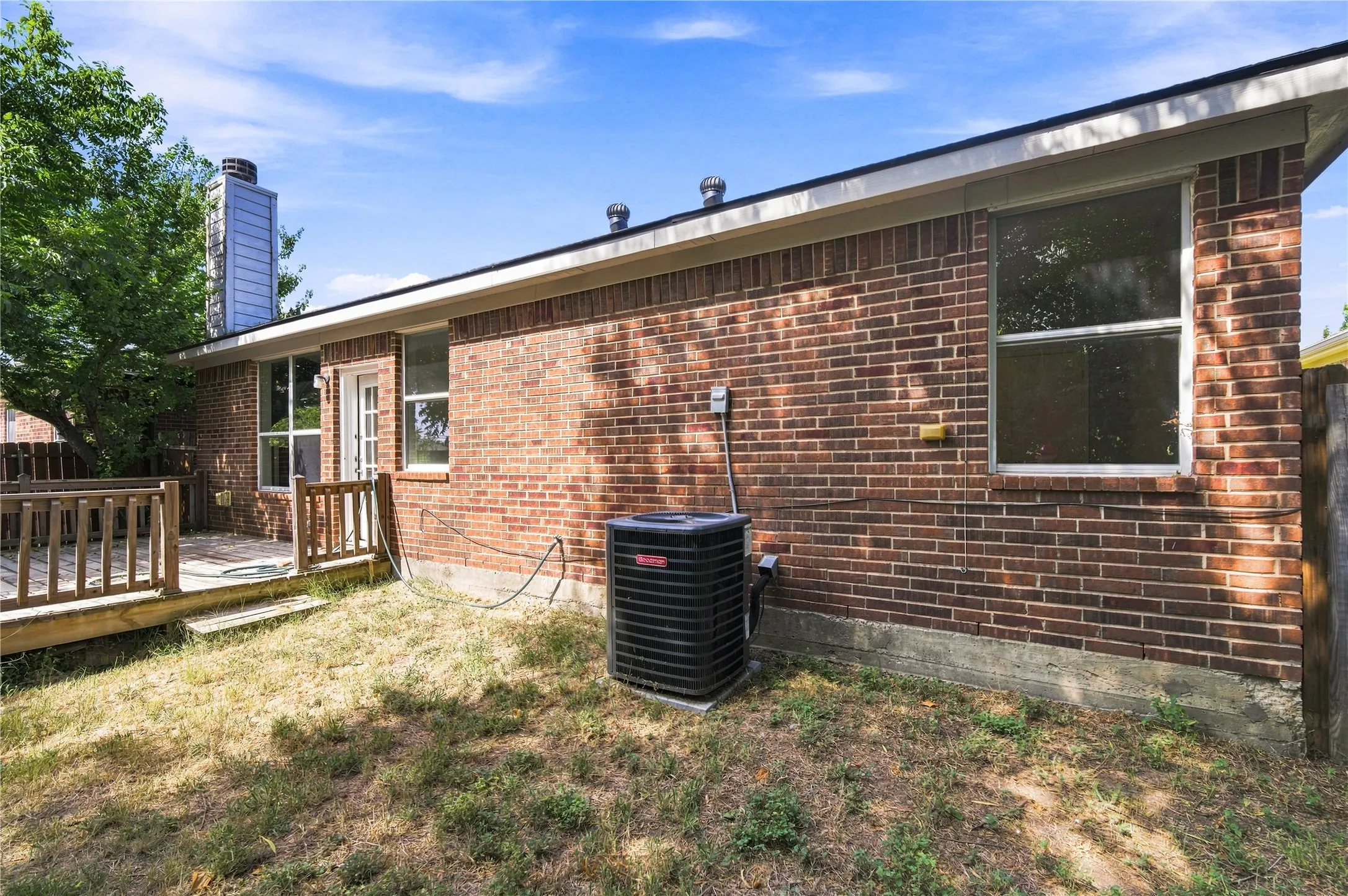 Brick exterior with multiple windows, an outdoor deck, and a central air conditioning unit