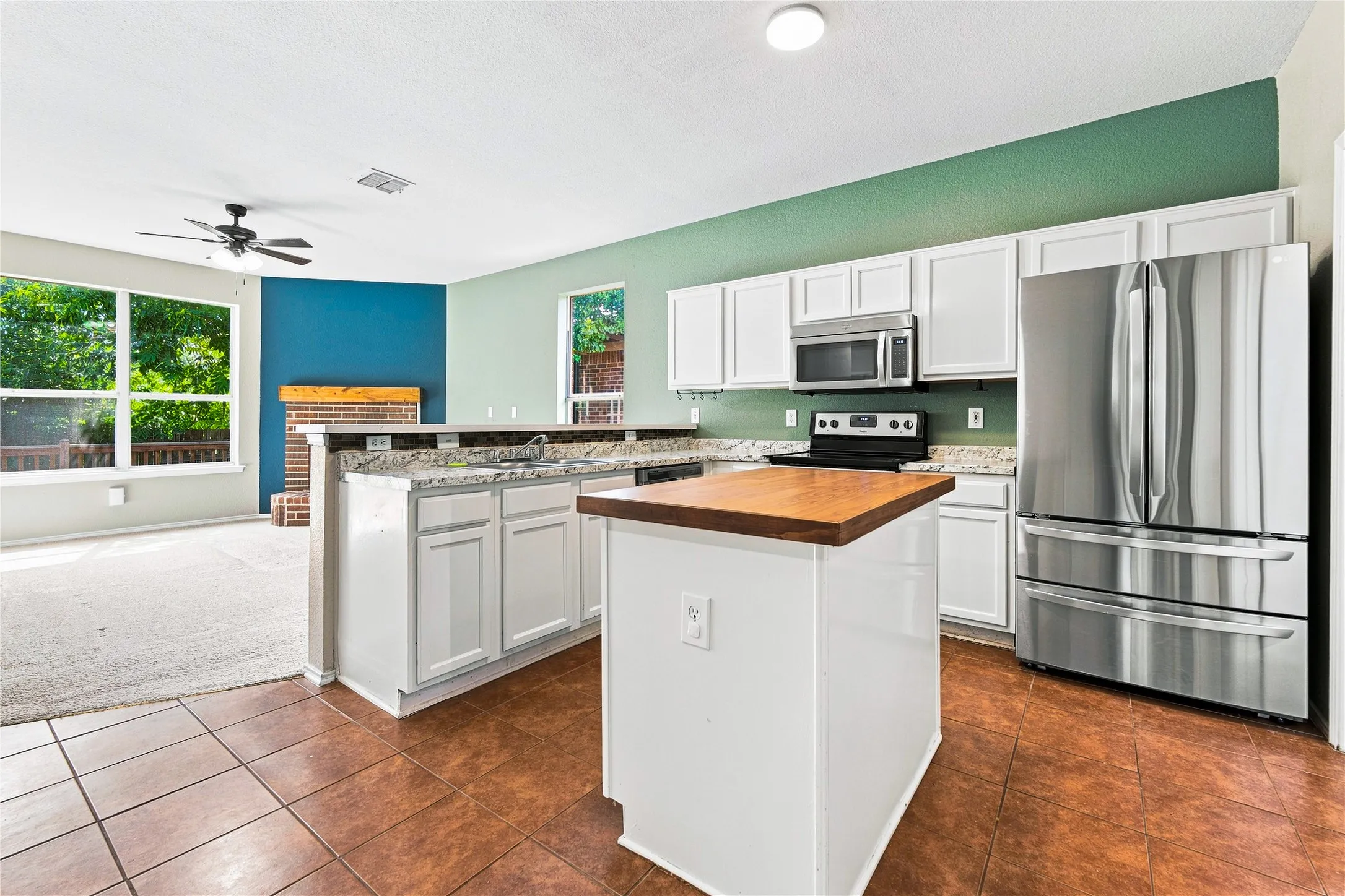 Kitchen featuring white cabinetry, stainless steel appliances, a center island with a wood-finish countertop, and tile flooring