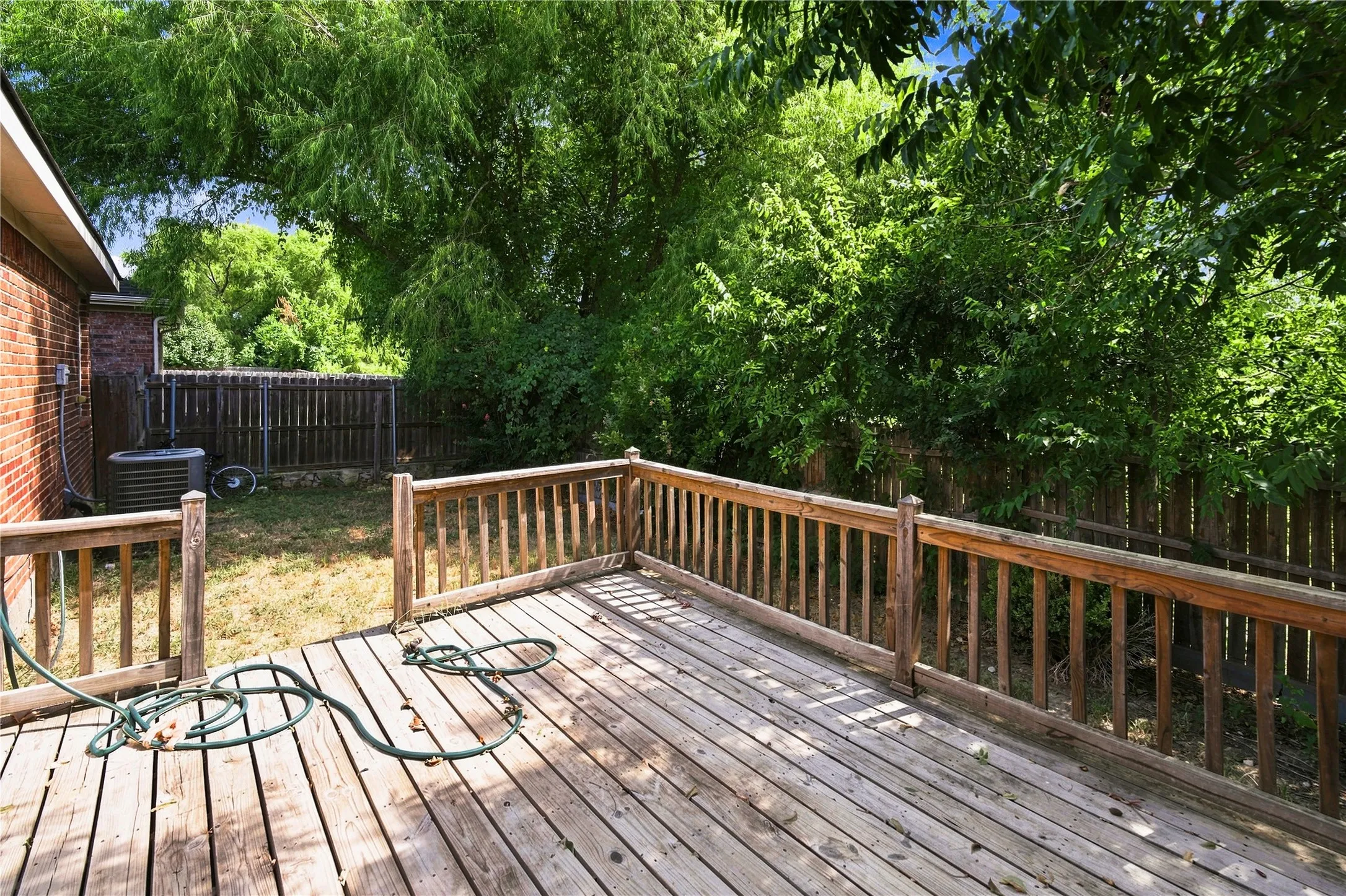Wood deck with wood railing, brick exterior, and mature perimeter trees