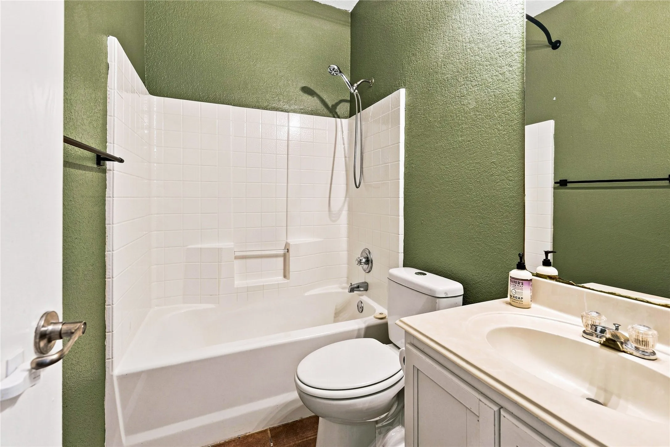 White tile shower surround with integrated soap dish, chrome shower fixture, and a white vanity with an integrated sink