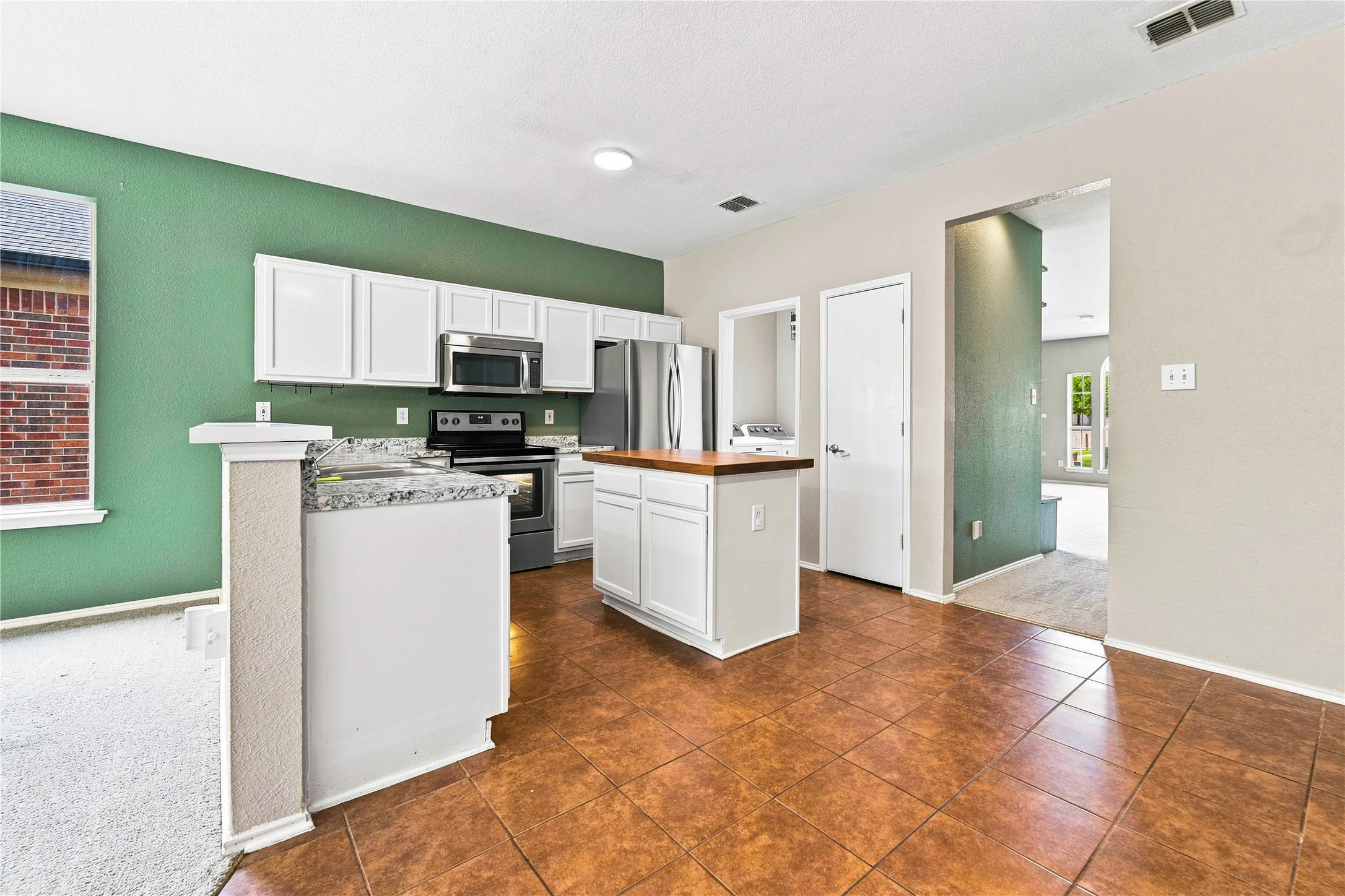 Kitchen featuring tile flooring, white cabinetry, stainless steel appliances, and a central island with a wood-finish countertop