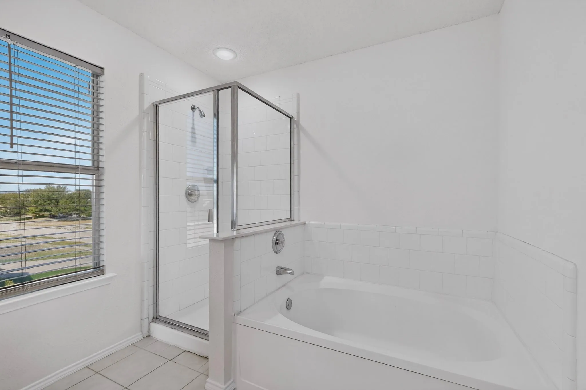 White tile shower enclosure with a glass door, built-in bathtub, and recessed lighting