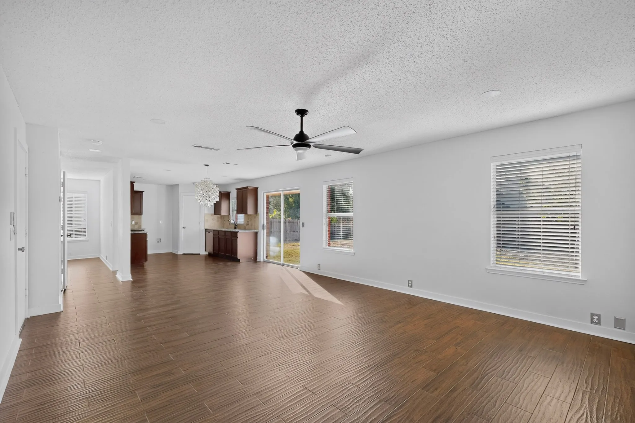 Open-concept living area featuring wood-finish flooring, a ceiling fan, and multiple windows. Adjacent to eat and kitchen.