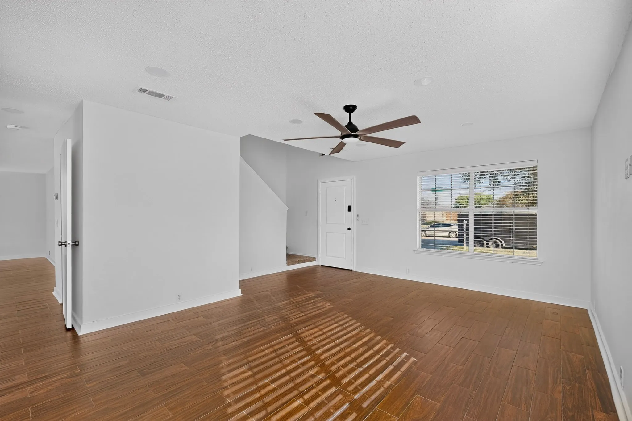 Spacious living area featuring wood-finish flooring, a ceiling fan with integrated lighting, and recessed ceiling lights