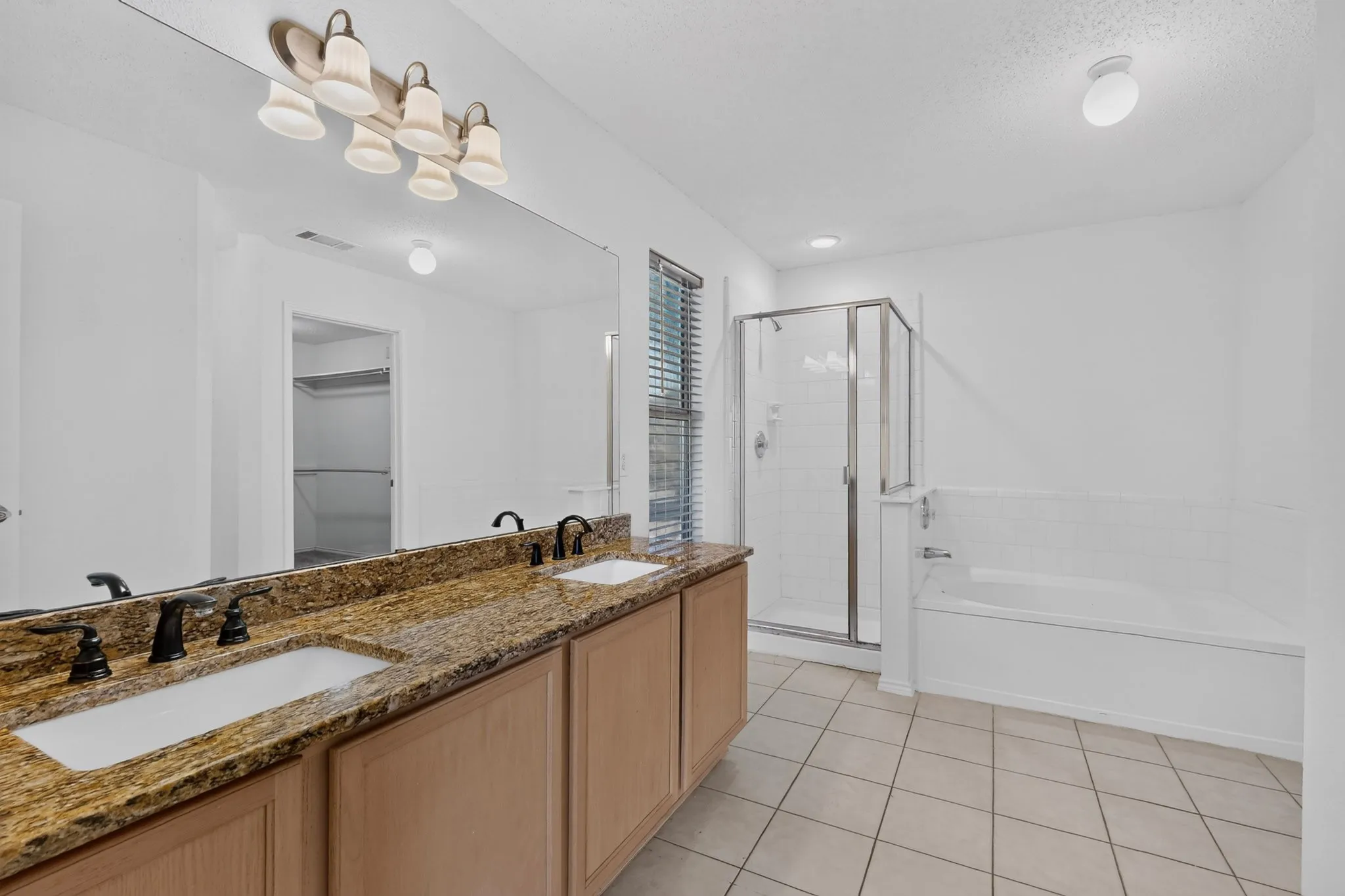 Dual vanity with granite countertop, separate shower, soaking tub, and tile flooring