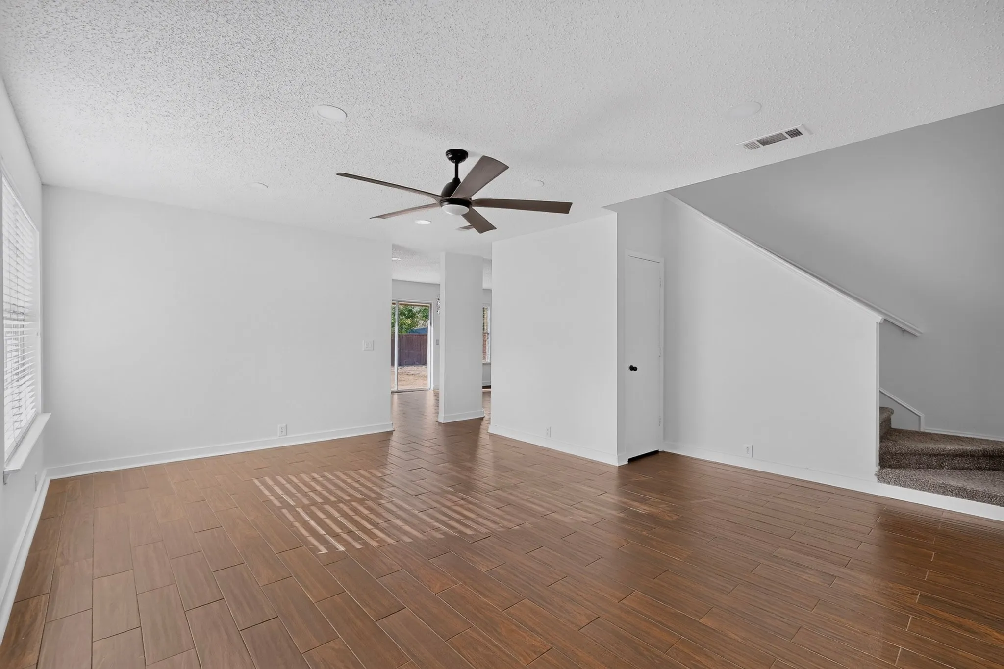 Wood-finish flooring, ceiling fan, recessed lighting and white walls.
