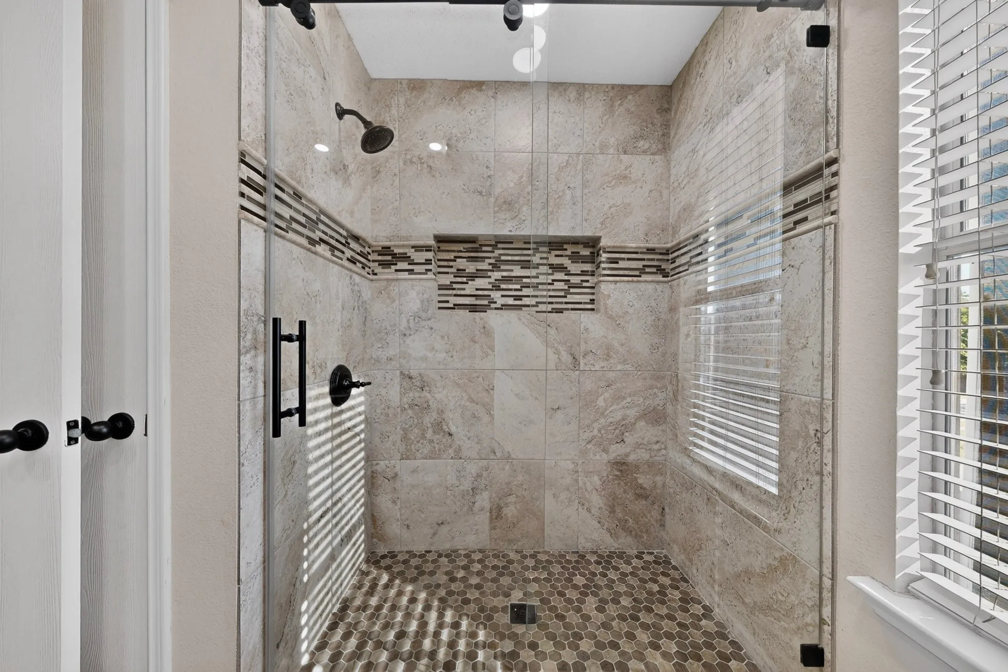 Walking-in glass-enclosed shower with a hex tile floor, tiled walls, a decorative mosaic accent, and a recessed niche
