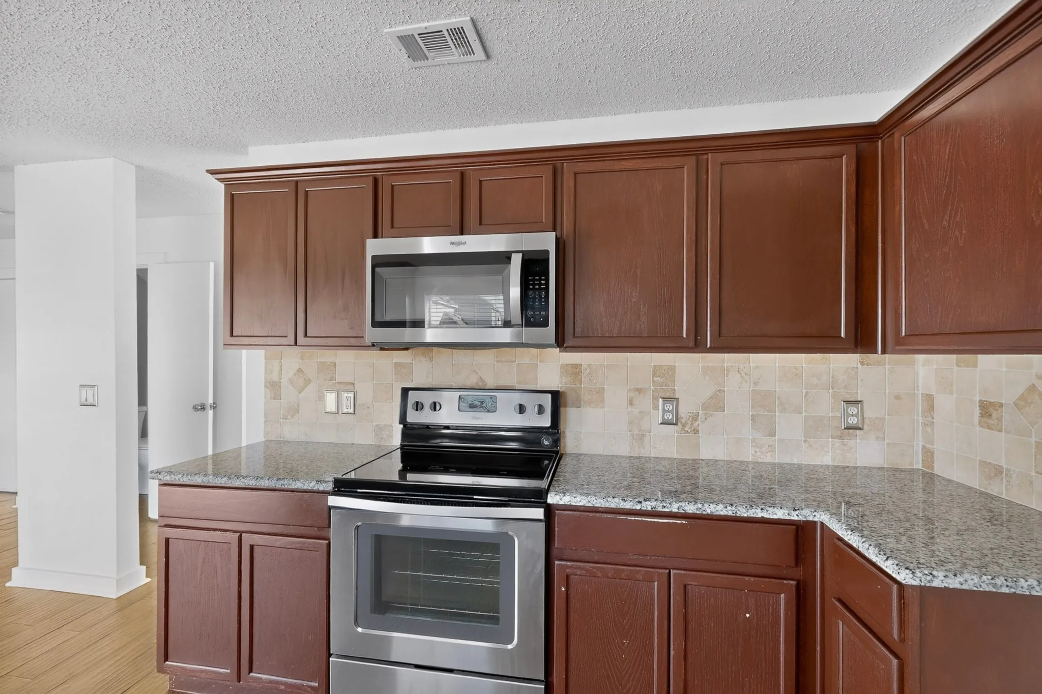 Kitchen featuring wood-finish cabinetry, stainless steel microwave, stainless steel range, mottled tile backsplash, and speckled countertops