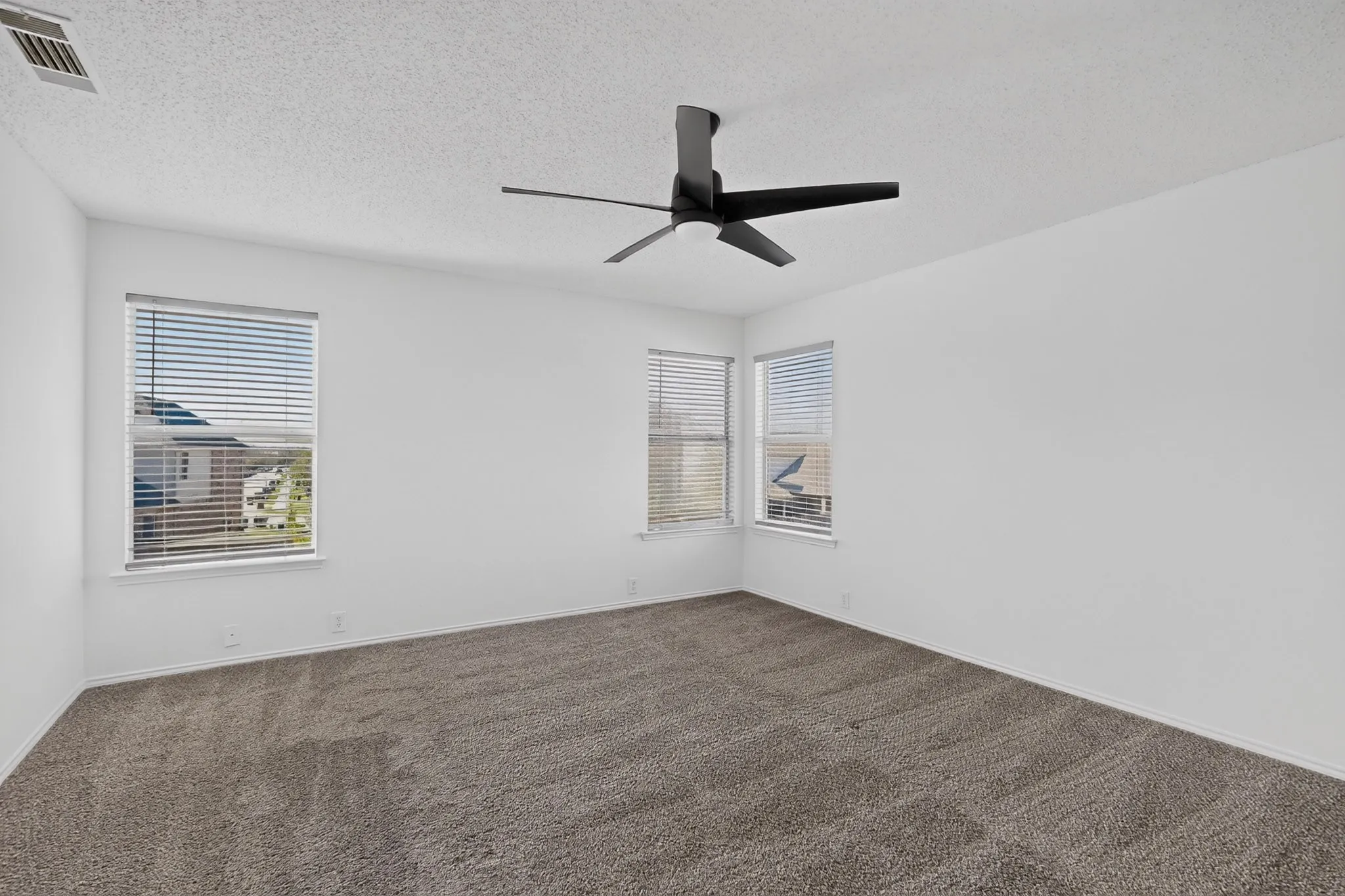Spacious primary bedroom with corner windows overlooking the back yard, lots of natural light, and upgraded ceiling fan.